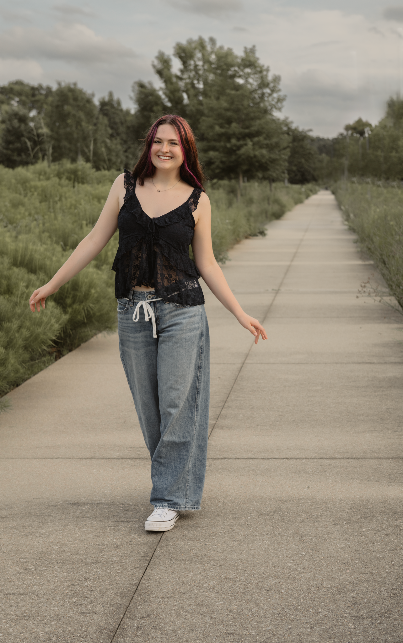 A candid shot of Haylee wearing a blue lace top  walking down a concrete path surrounded by greenery during her senior session