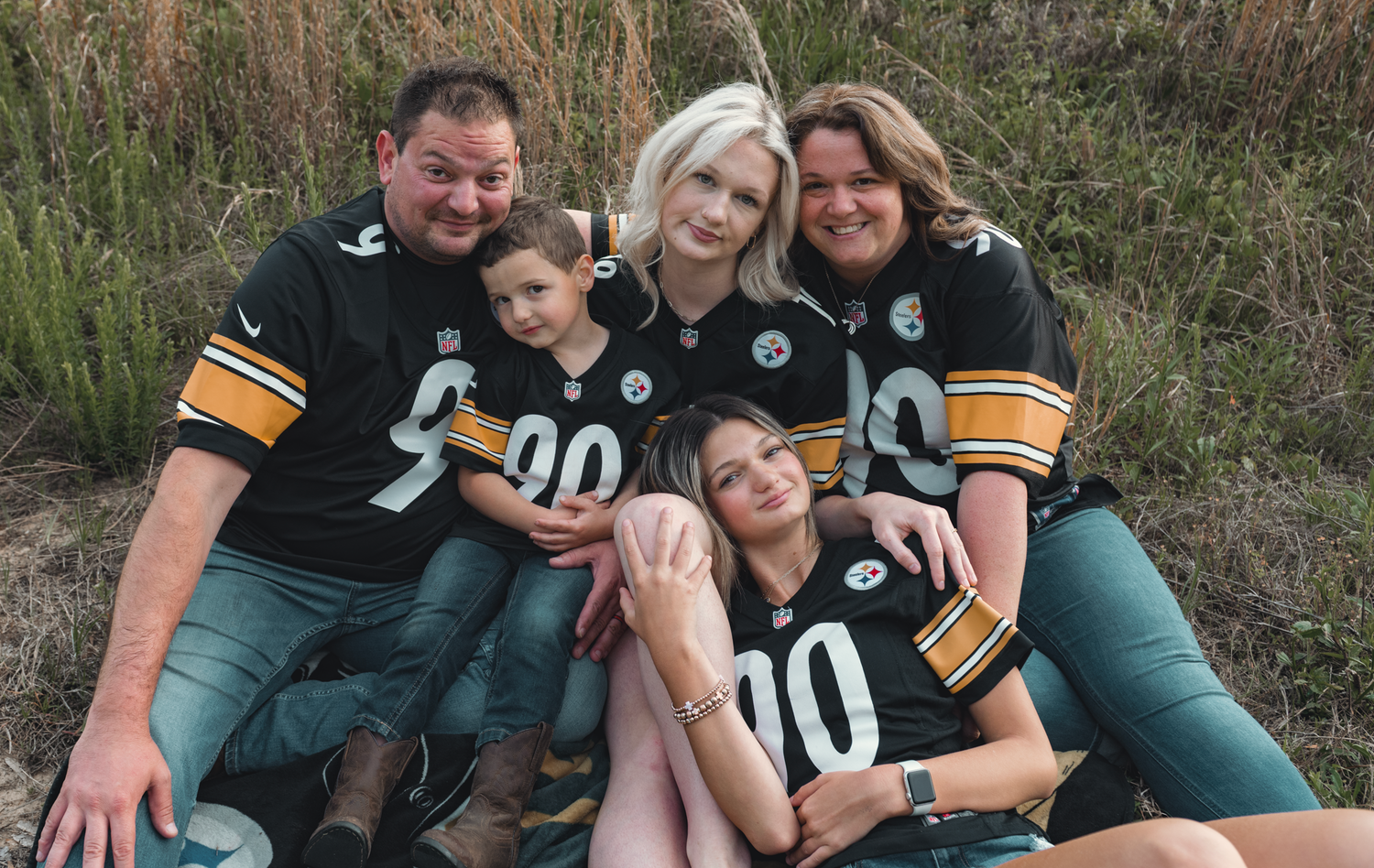 A family wearing matching black and gold sports jerseys poses together outdoors on grass.