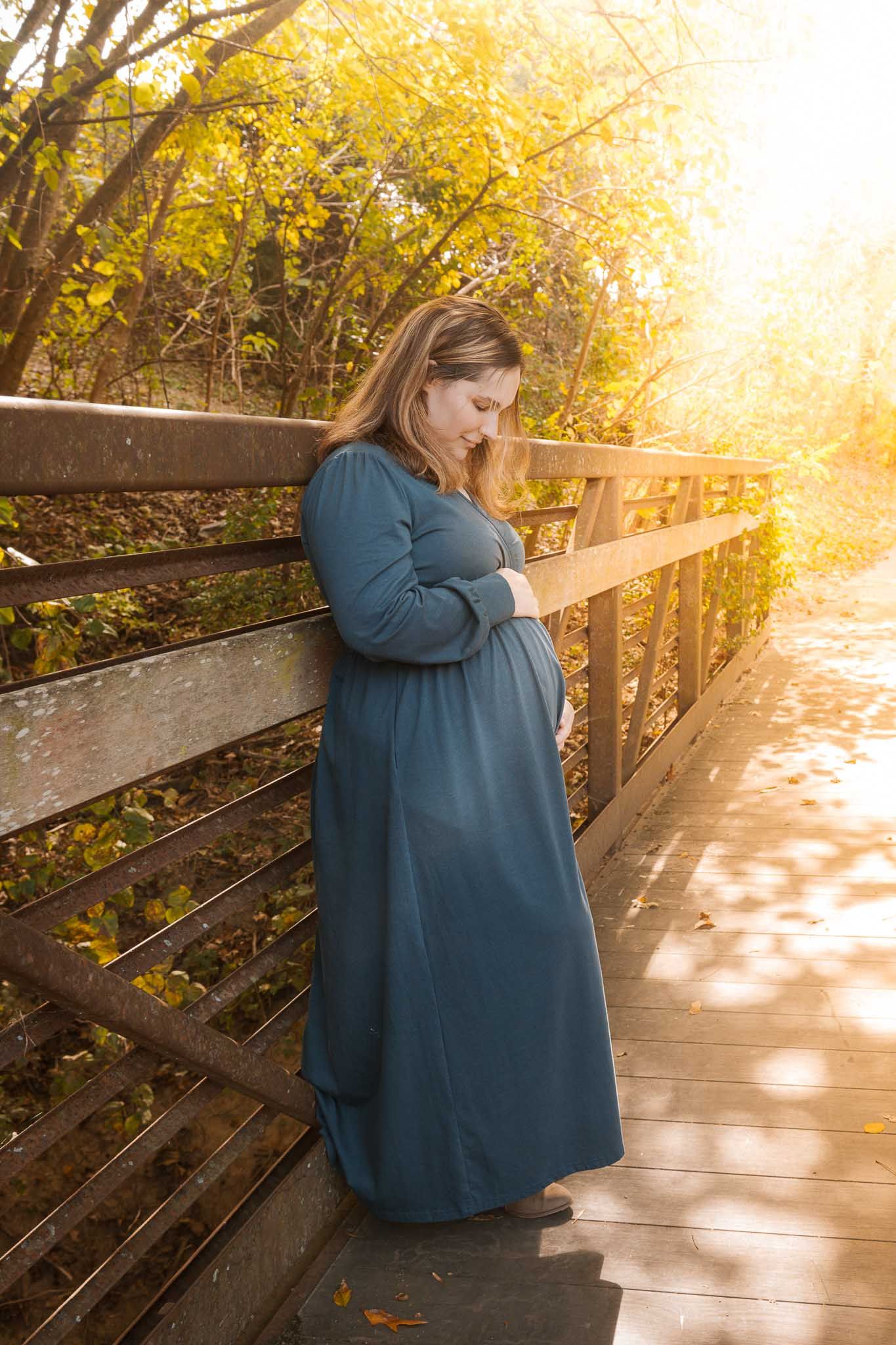 Person in blue coat sits on wooden boardwalk surrounded by golden autumn foliage at sunset.