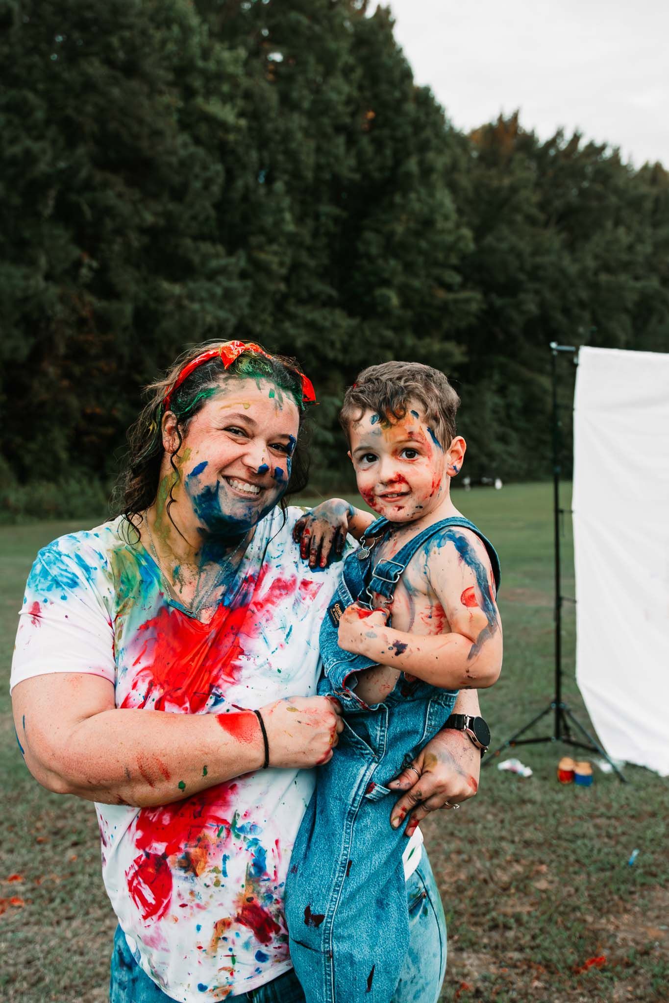 Two people covered in colorful paint smile together outdoors during a messy fun paint activity.