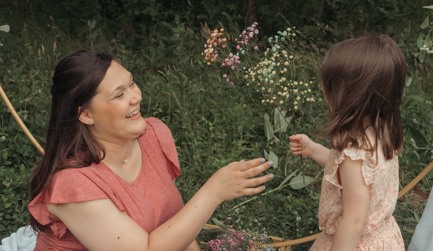 Two people share a joyful outdoor moment while sitting among flowering plants in a garden setting.