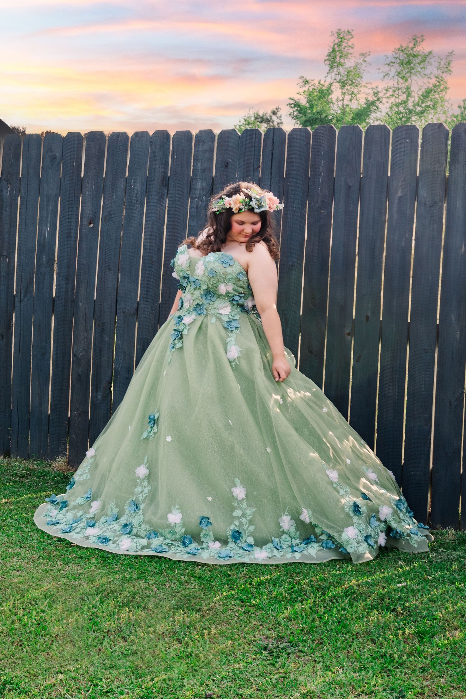 High school senior wearing mint green ballgown with blue floral details against wooden fence at sunset in Smithfield, NC.