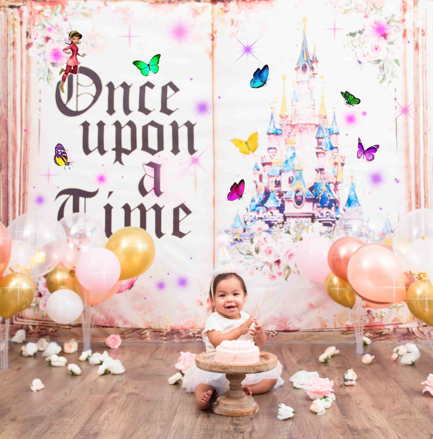 Dreamy fairytale backdrop with colorful butterflies, balloons, and a castle features a decorated wooden cake smash setup.