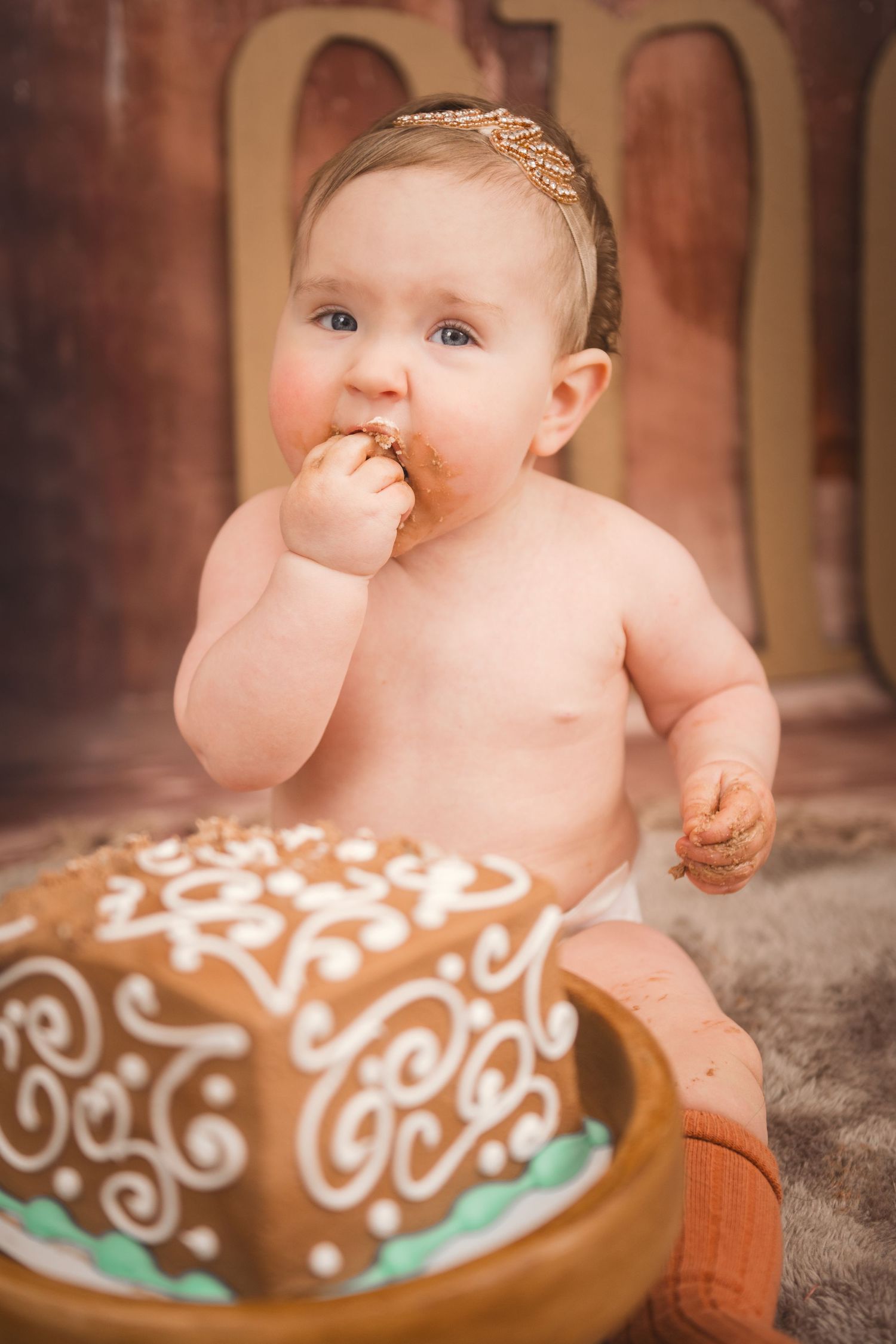 Baby enjoying a smash cake with ornate white frosting decorations during a first birthday photoshoot in Smithfield, NC by Krystie Nicole