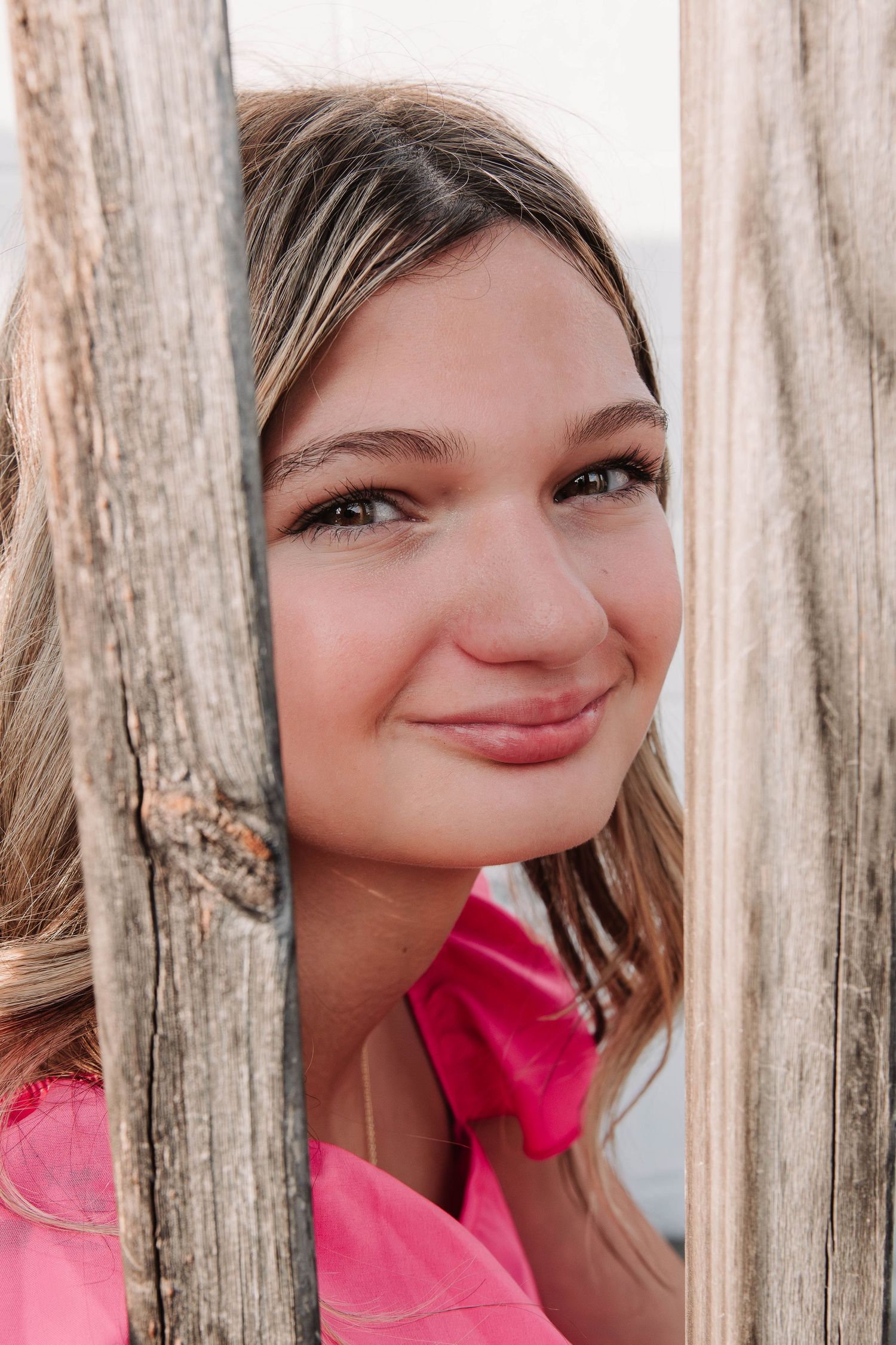 Creative portrait through wooden posts in natural lighting wearing a bright pink top.