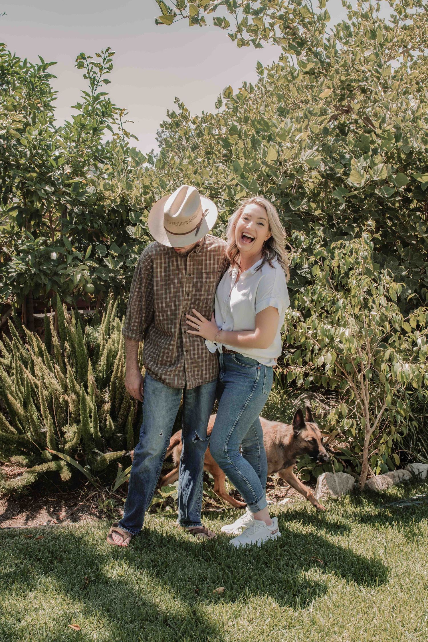 A romantic couple shares a candid moment together in a sunny orchard garden setting.
