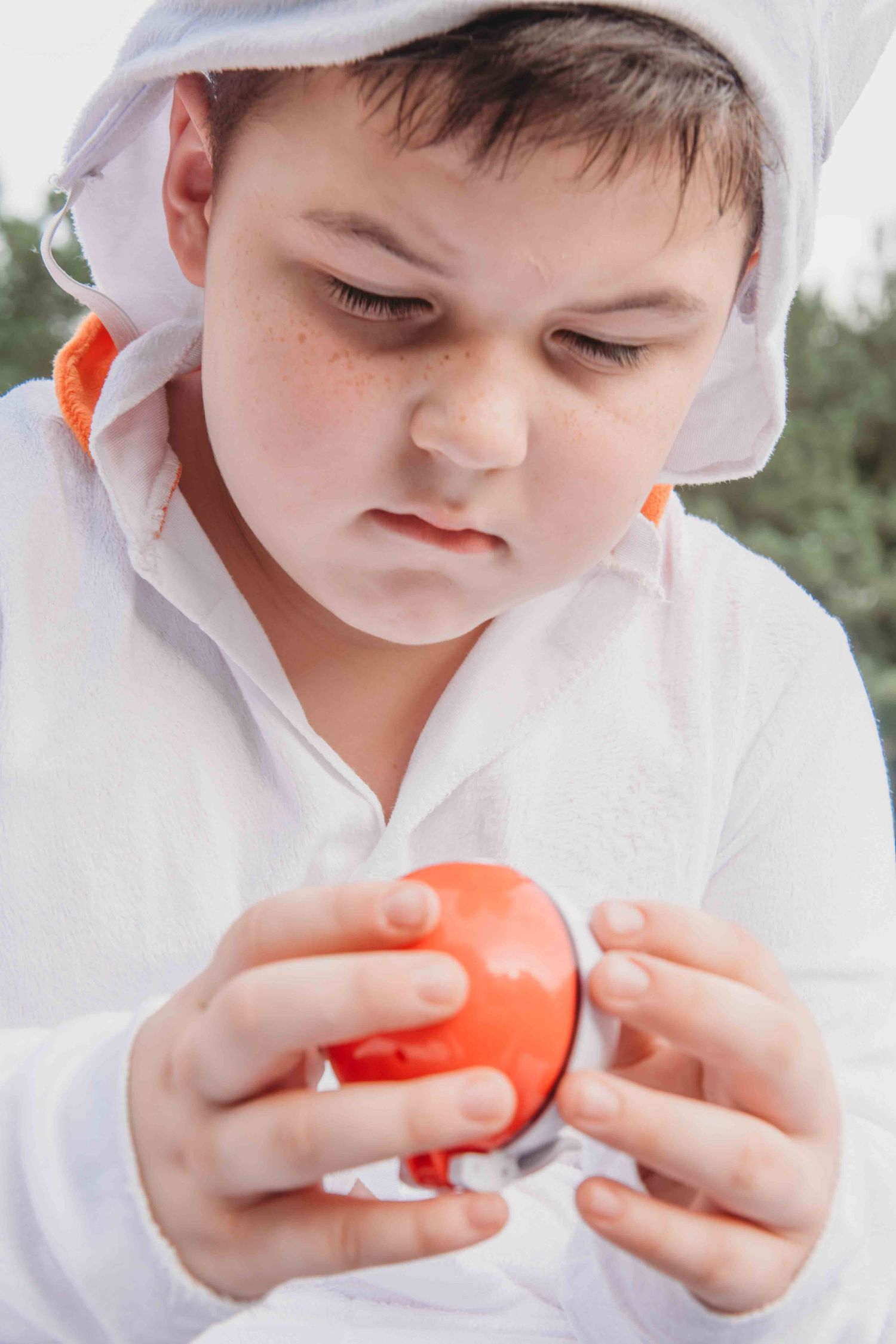 A young figure in a white hoodie examines a bright orange tomato with focused concentration.