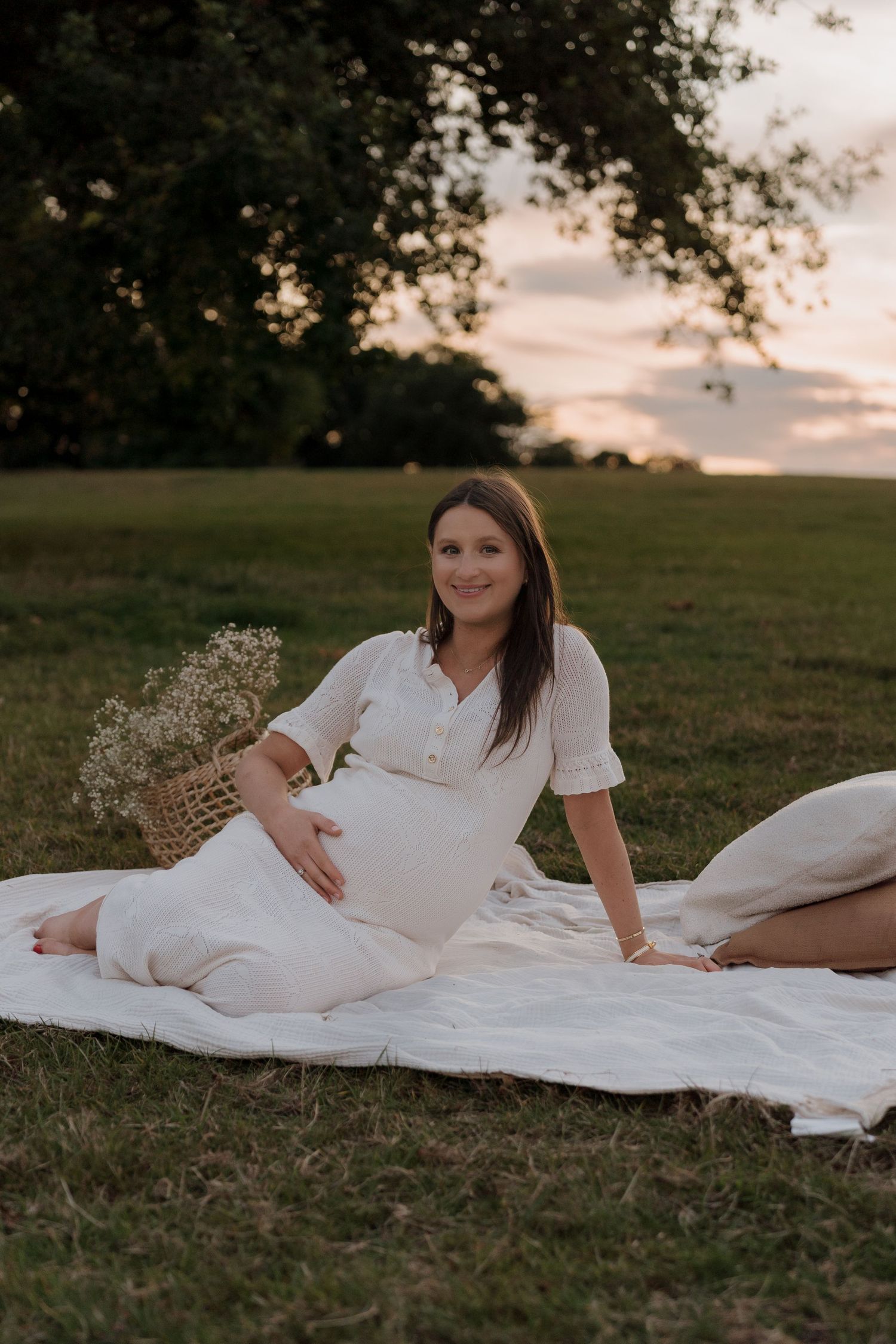 A person in a white dress rests on a blanket in a grassy field during sunset.