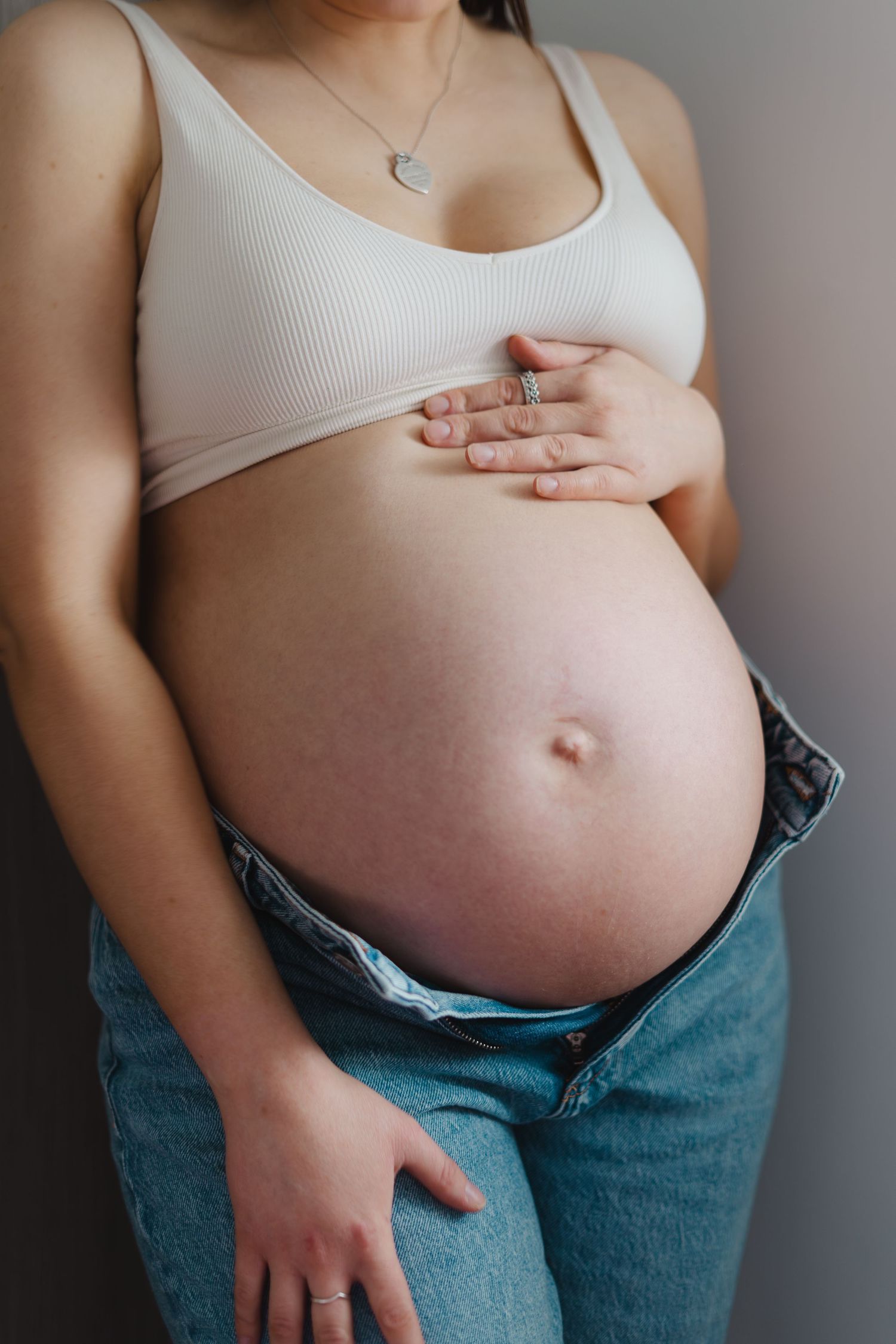 A sequence of pregnancy progression photos showing a growing belly with hands cradling the bump in blue jeans.