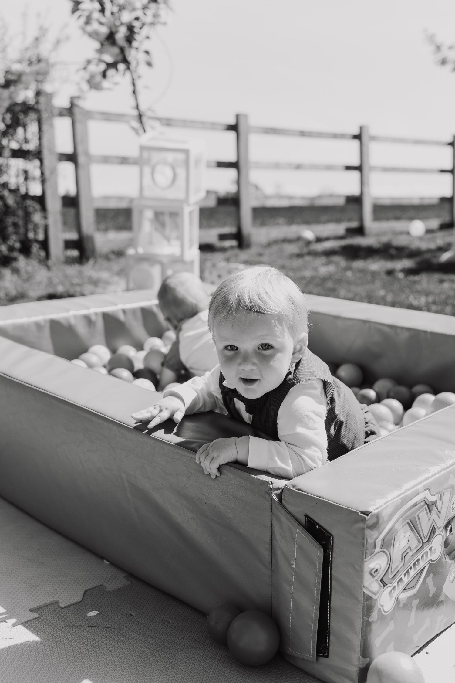A small child peeks over the edge of a cardboard box in a black and white photo series.