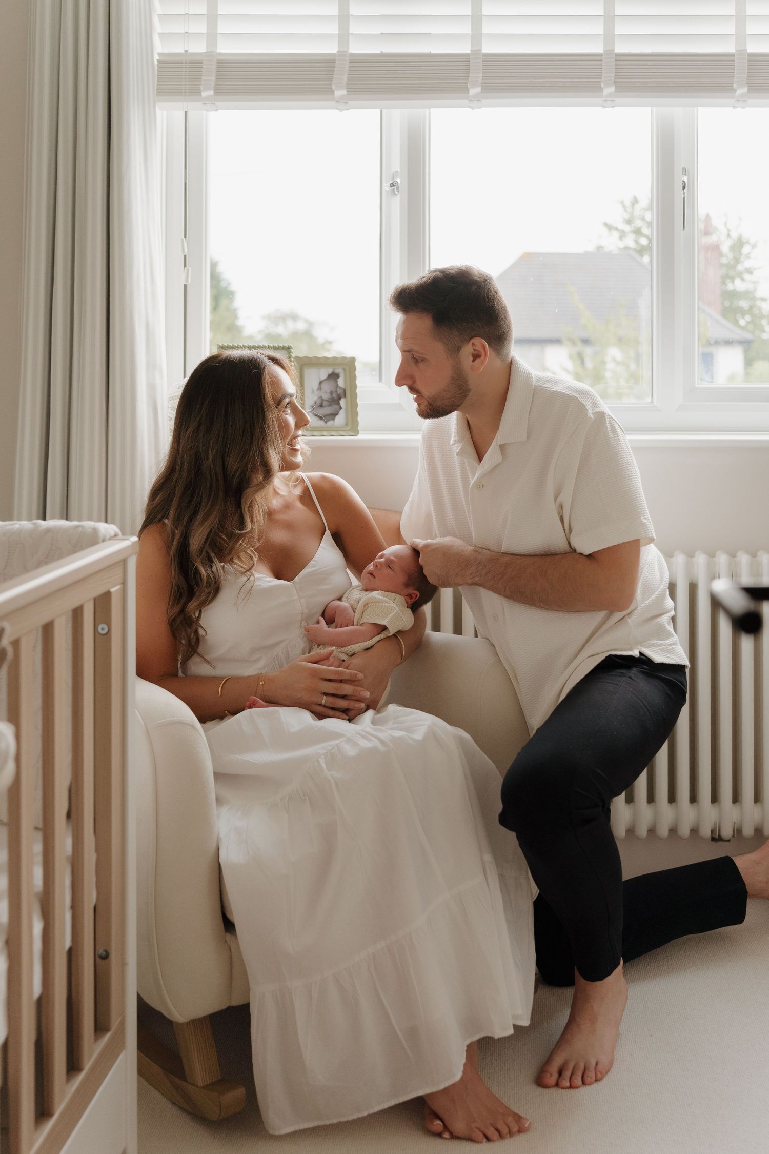 A couple in white clothing shares tender moments together while sitting in a bright sunlit room.