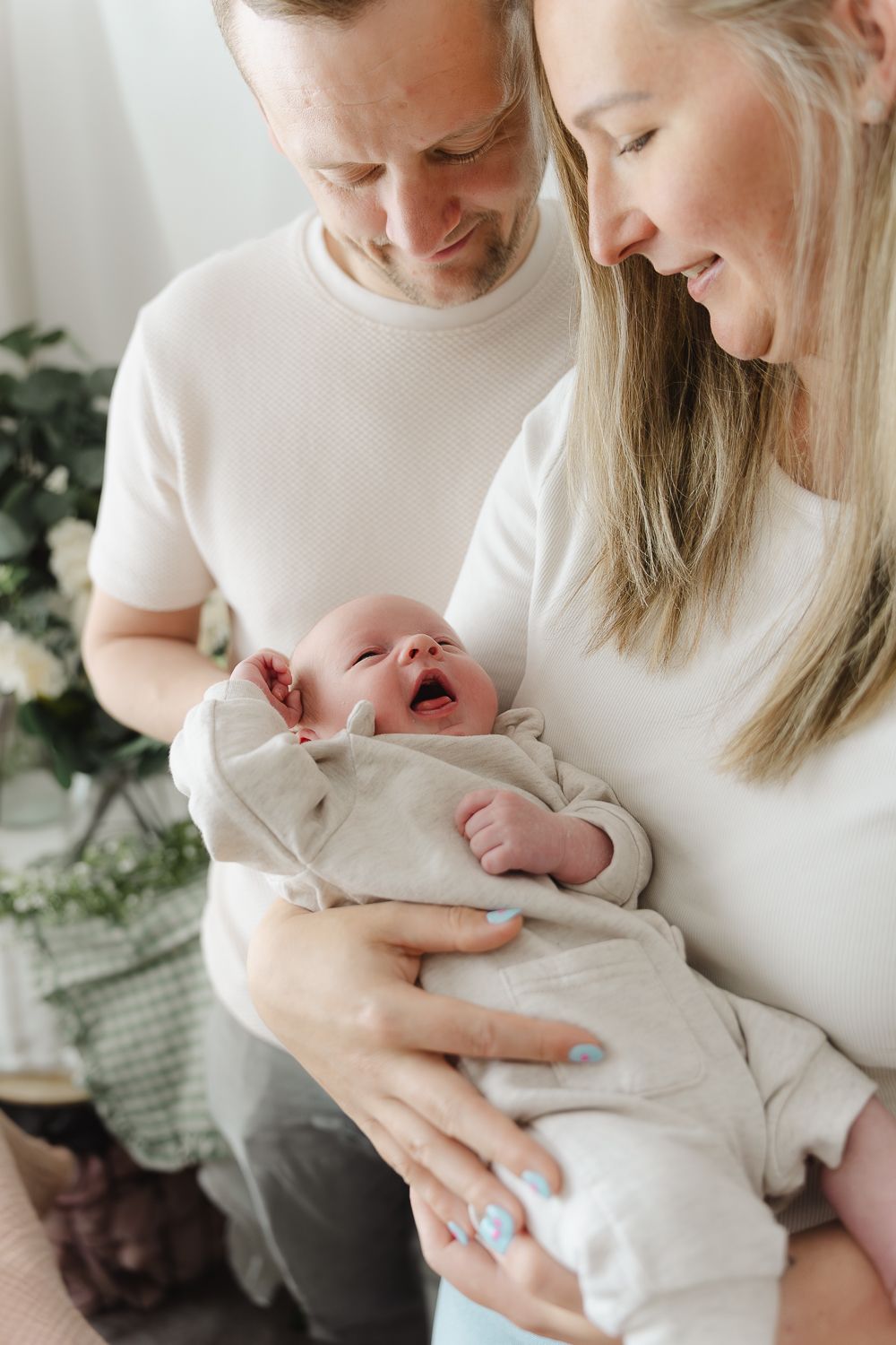 A tender moment between parent and newborn baby wearing white clothing in a bright indoor setting.