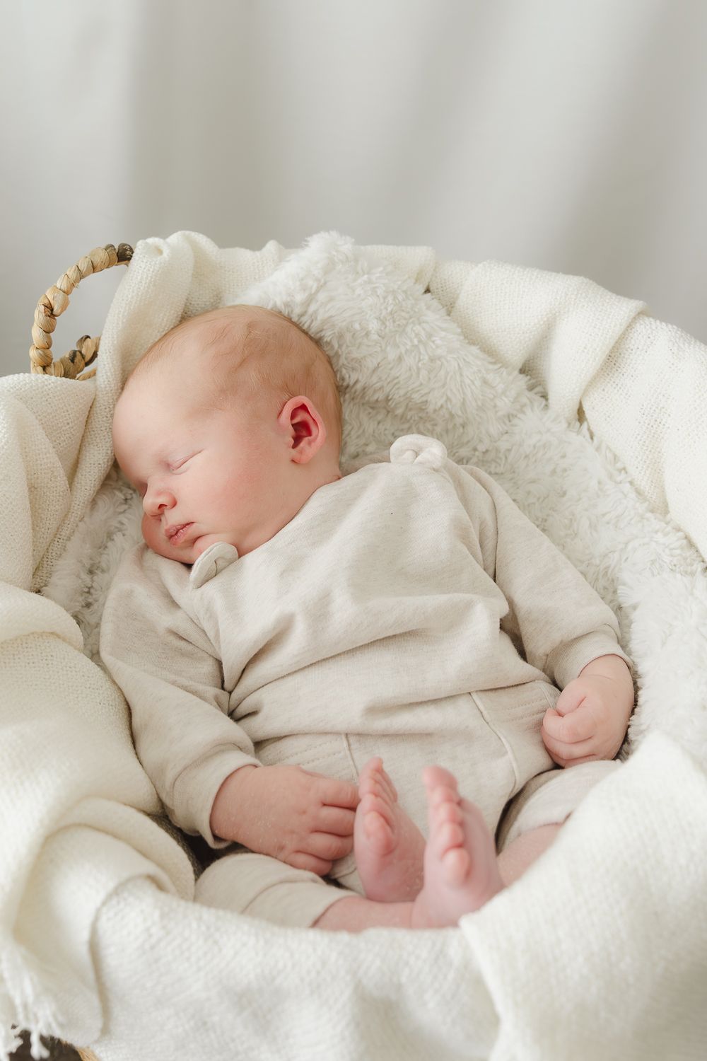Sleeping newborn in cream colored outfit rests peacefully on white blanket.
