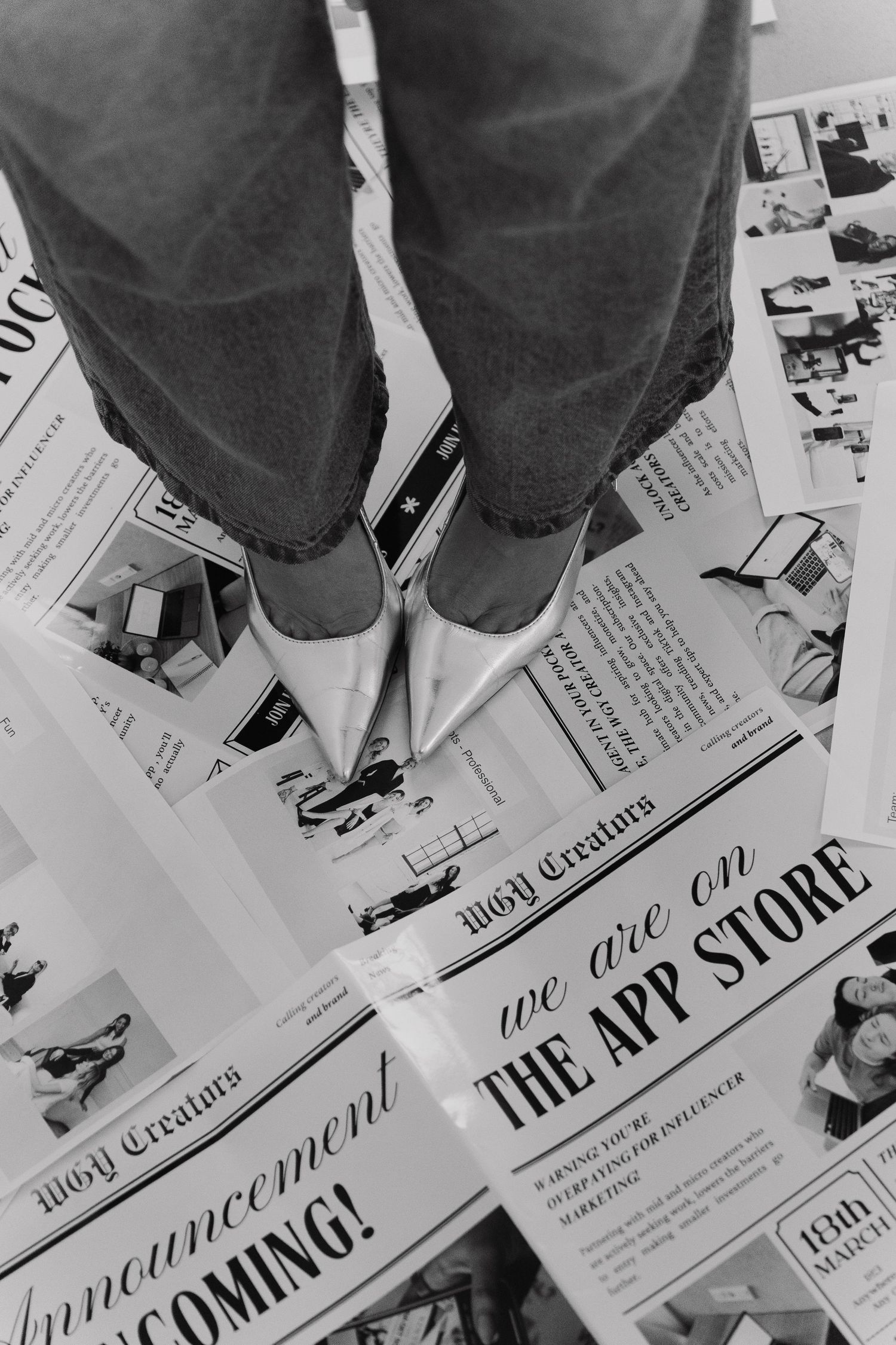 Black and white photo of feet in white shoes standing on vintage newspaper advertisements.