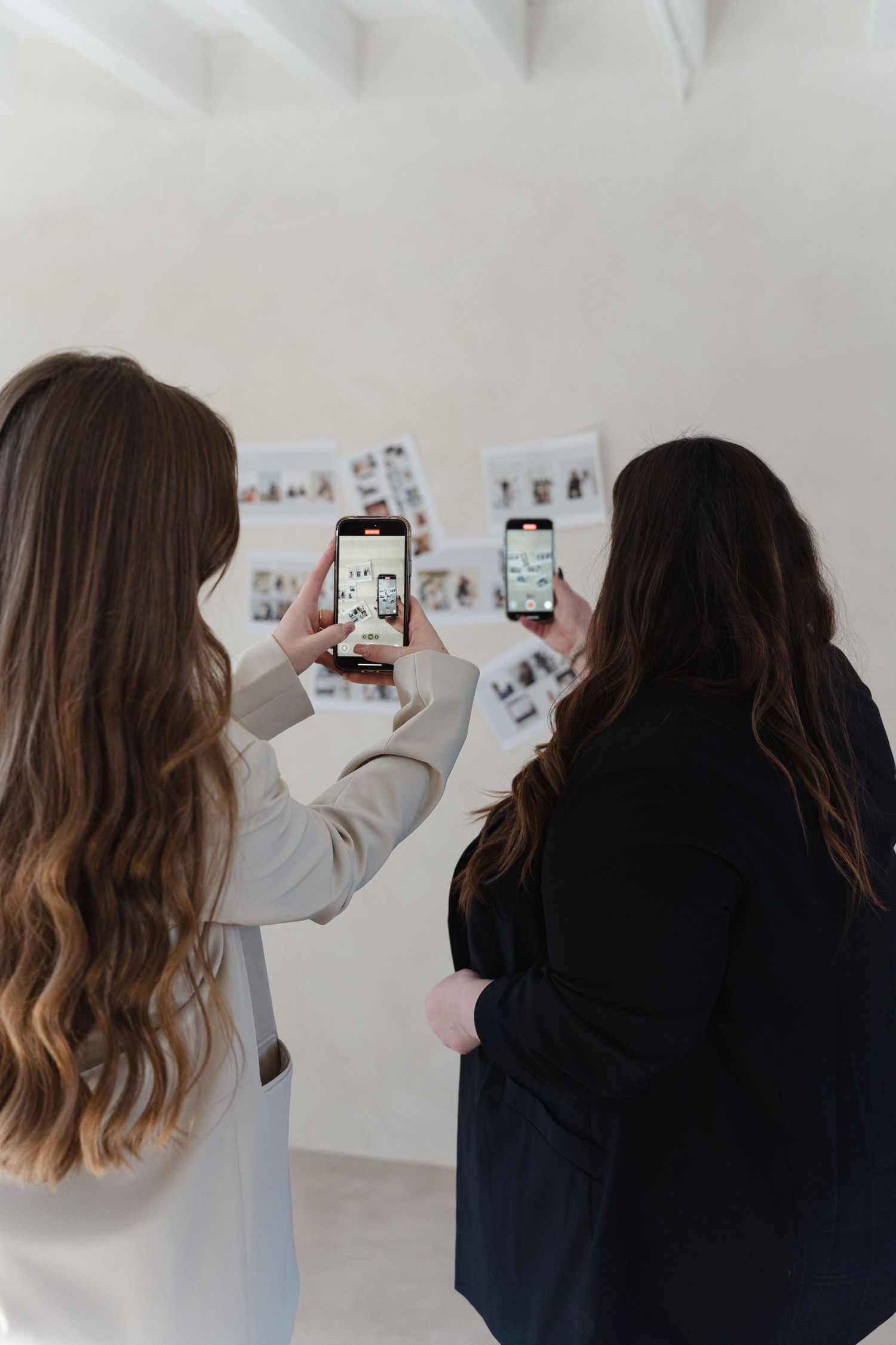 Multiple people photographing artwork on gallery walls with smartphones in a museum or exhibition space.