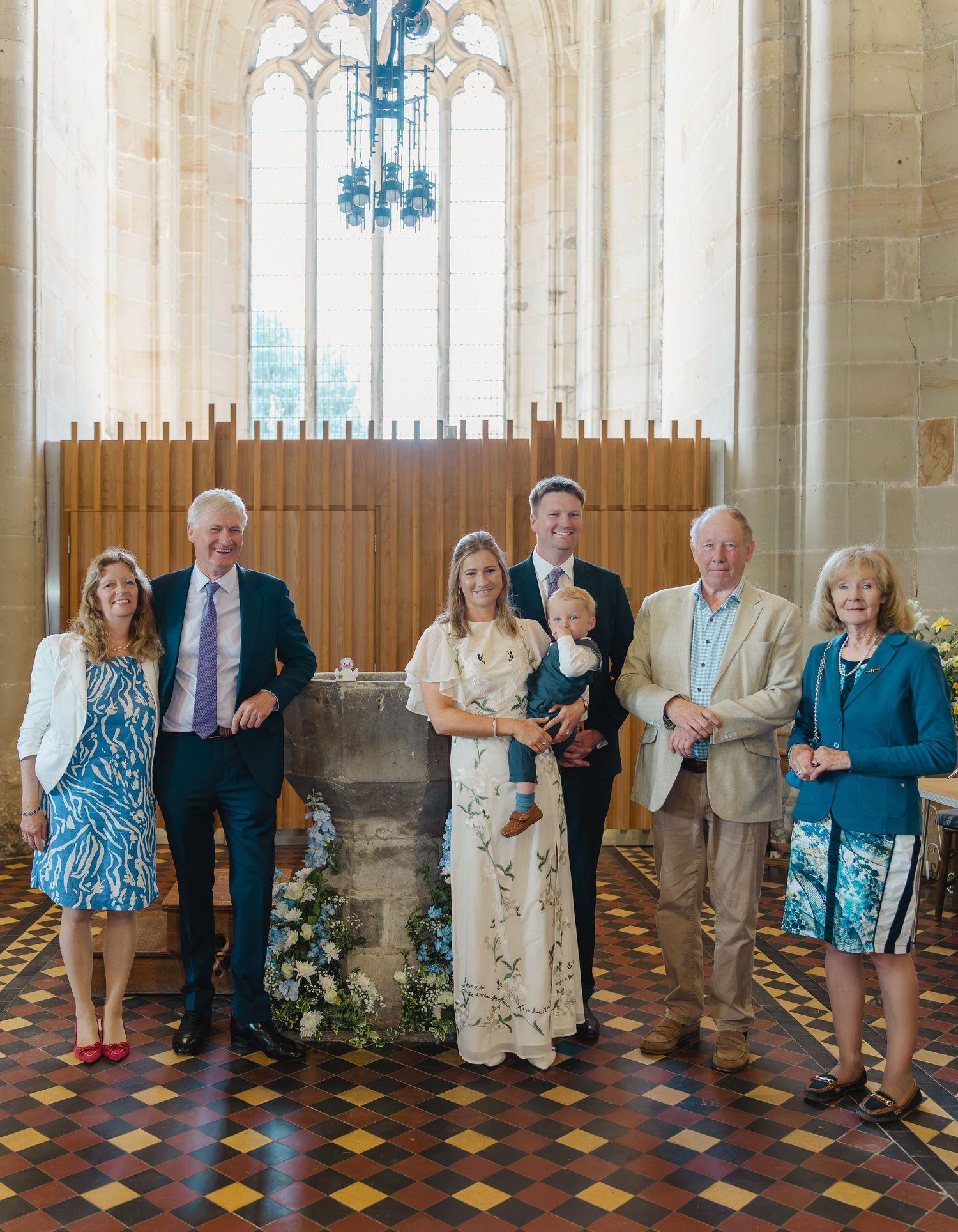 A group of people stand in a line against a stone wall with ornate windows in what appears to be a church or cathedral.