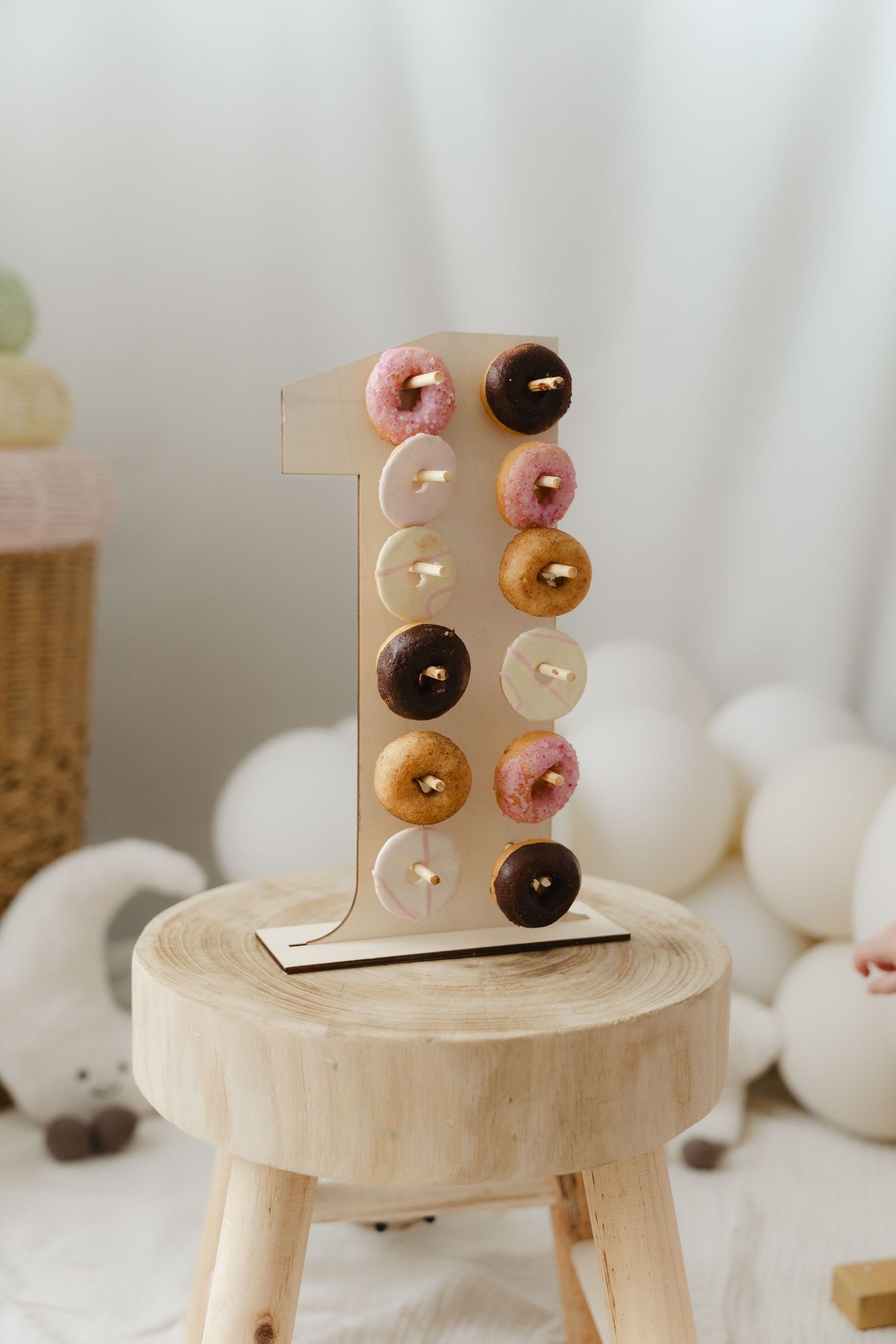 Wooden donut display stands showcase colorful glazed donuts against a white background in a minimalist setting.