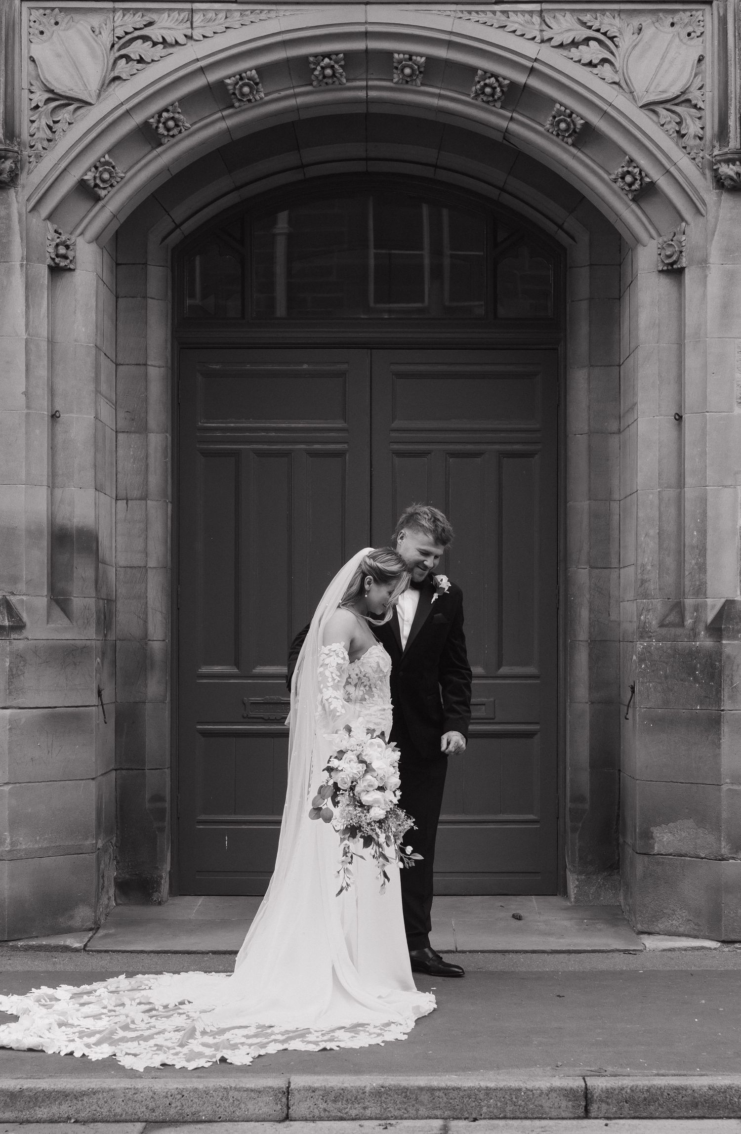 Four black and white wedding photos show a couple in formal attire posing in front of ornate stone archways.
