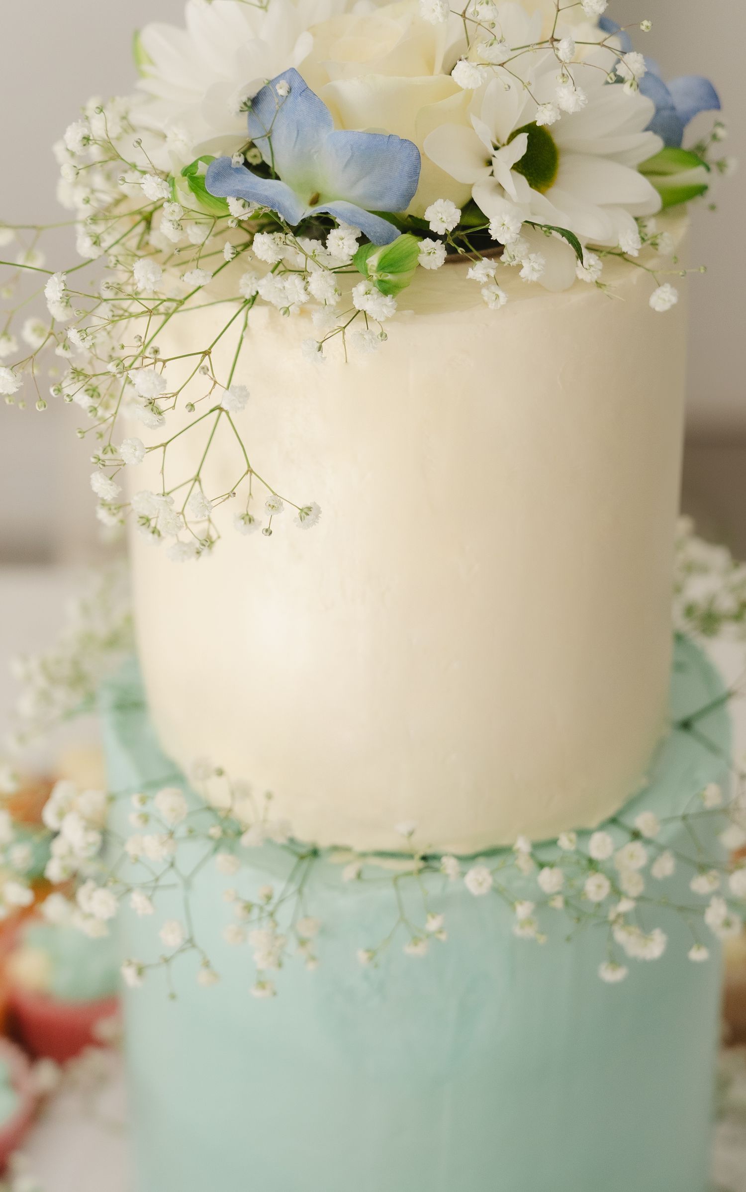 A close-up view of a two-tiered wedding cake decorated with white flowers and baby's breath on a mint green base.