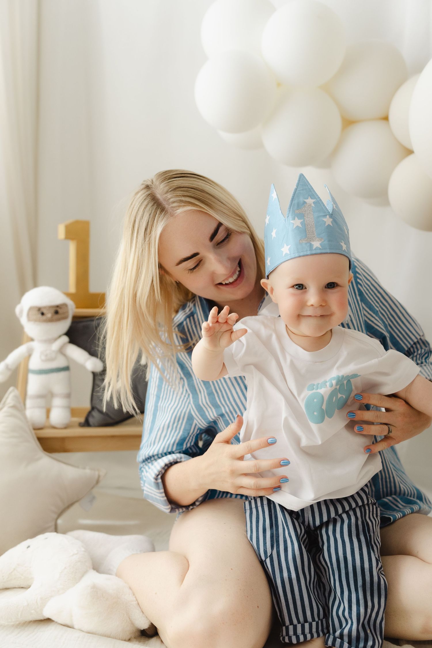 A parent and baby in matching white outfits share joyful moments while playing with balloons and decorations.