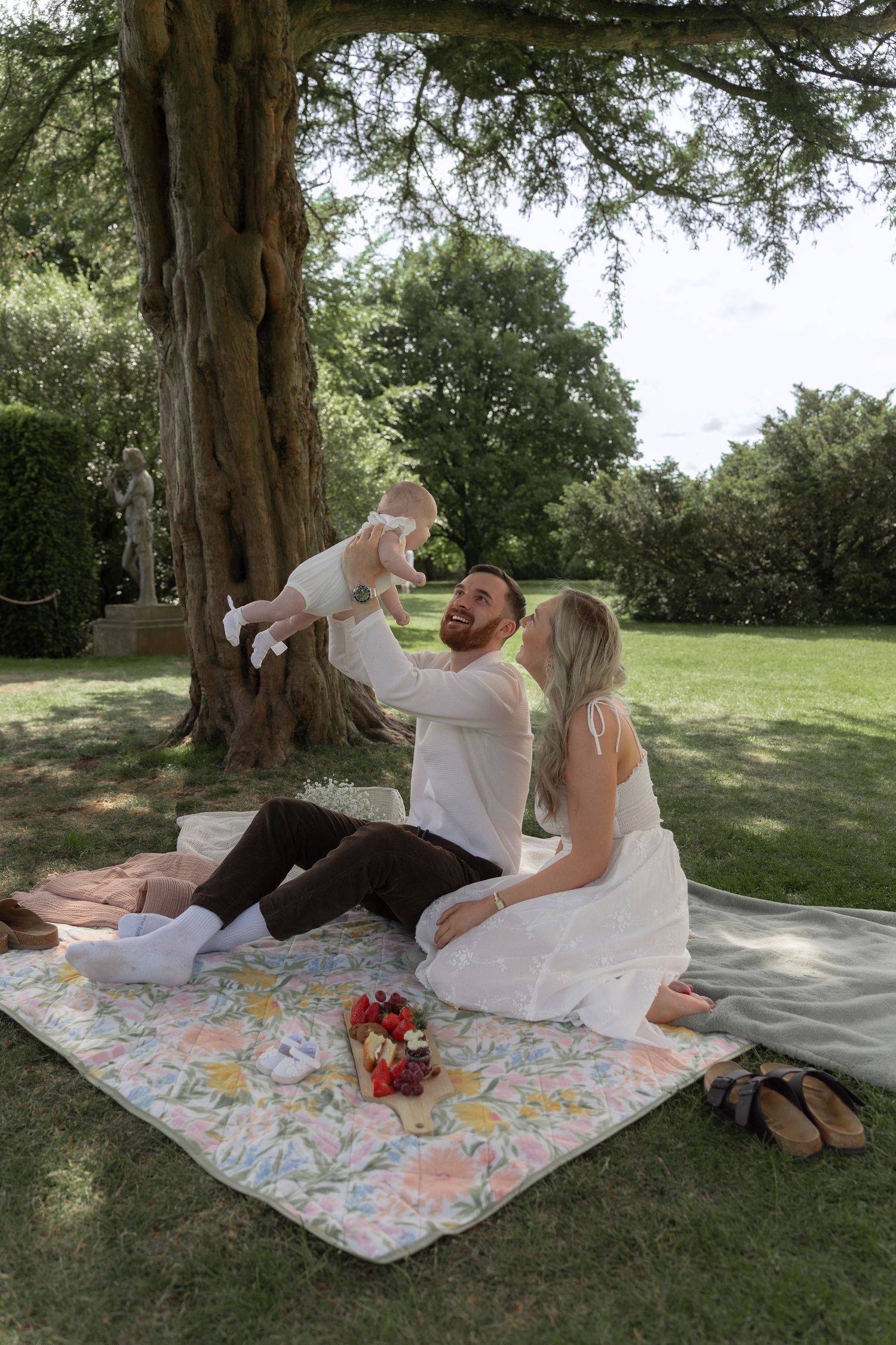 Couple enjoying a romantic picnic under a large tree on a floral patterned blanket.