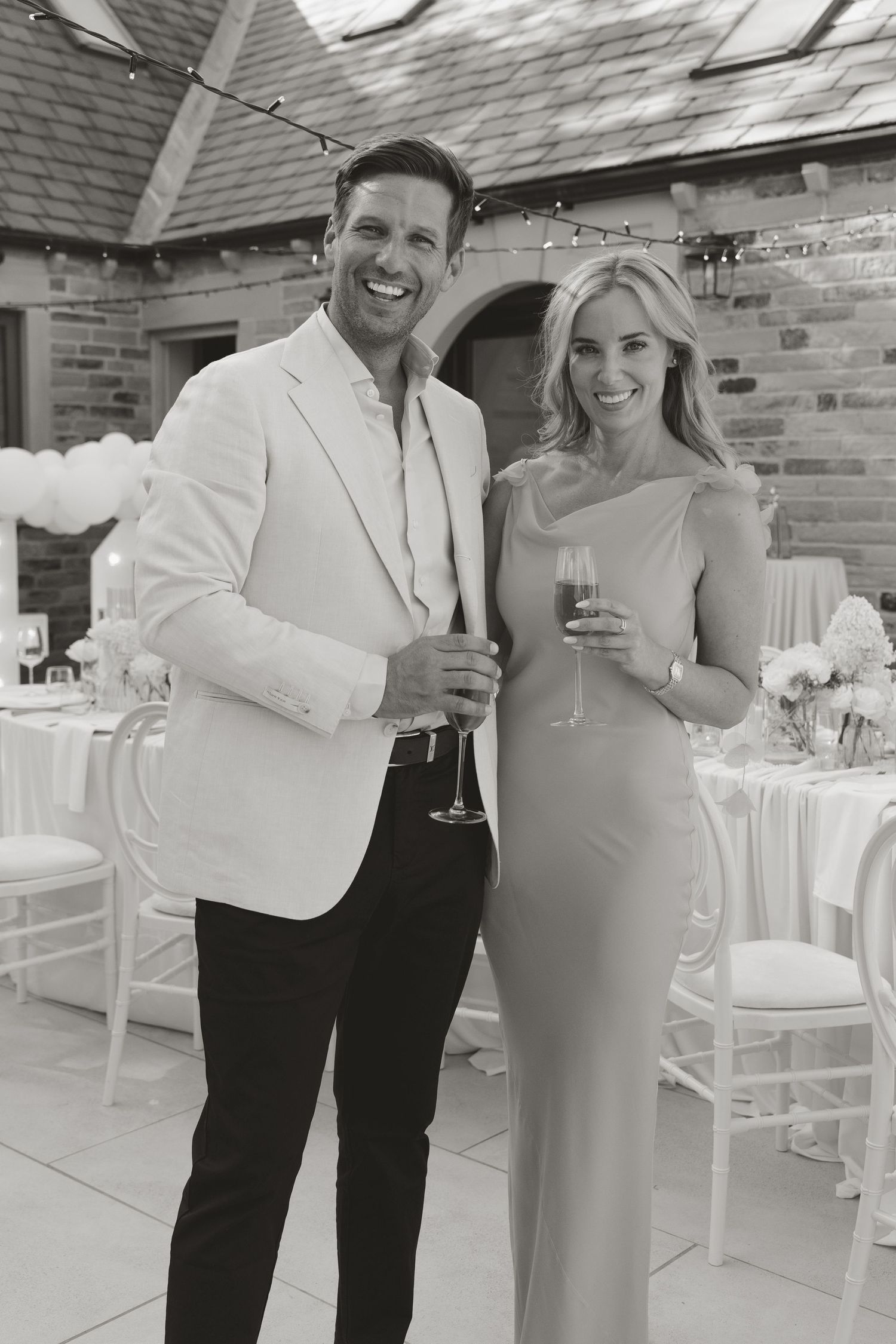 A smiling couple in elegant attire toasting with champagne glasses at an outdoor wedding reception venue.