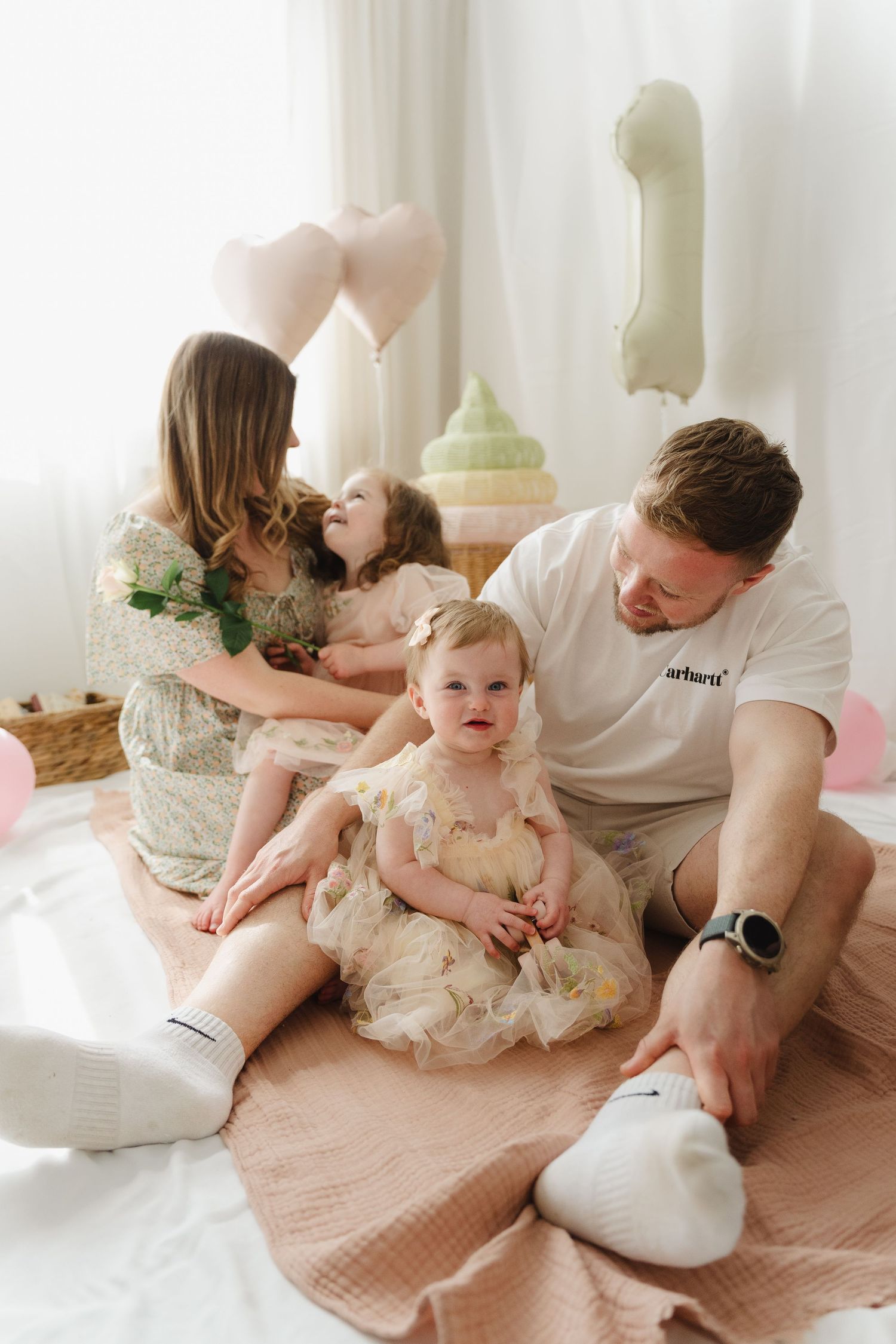 Family lying on pink blanket during intimate lifestyle photoshoot in bright minimalist setting.