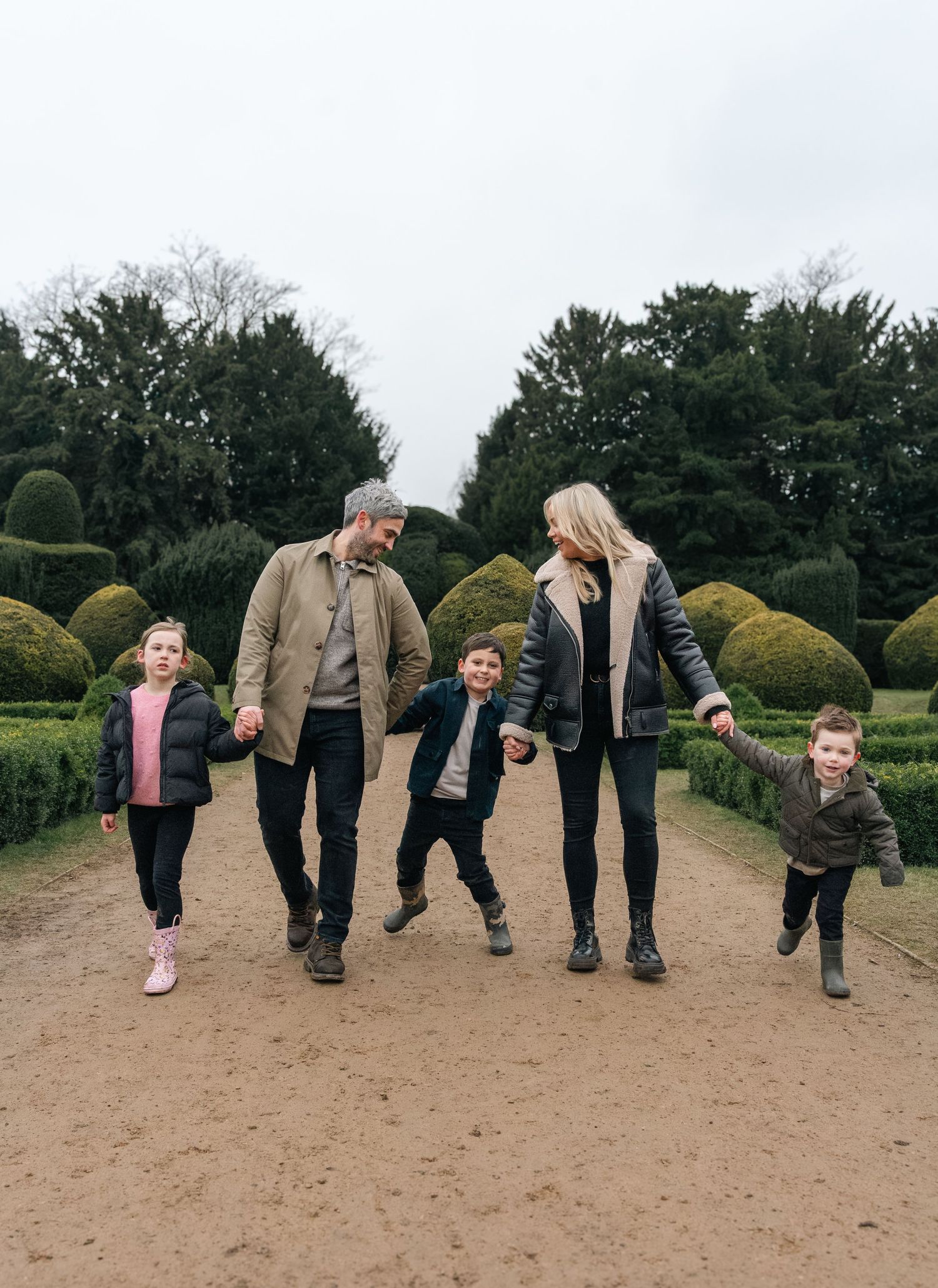 Family walking together on garden path surrounded by manicured hedges.