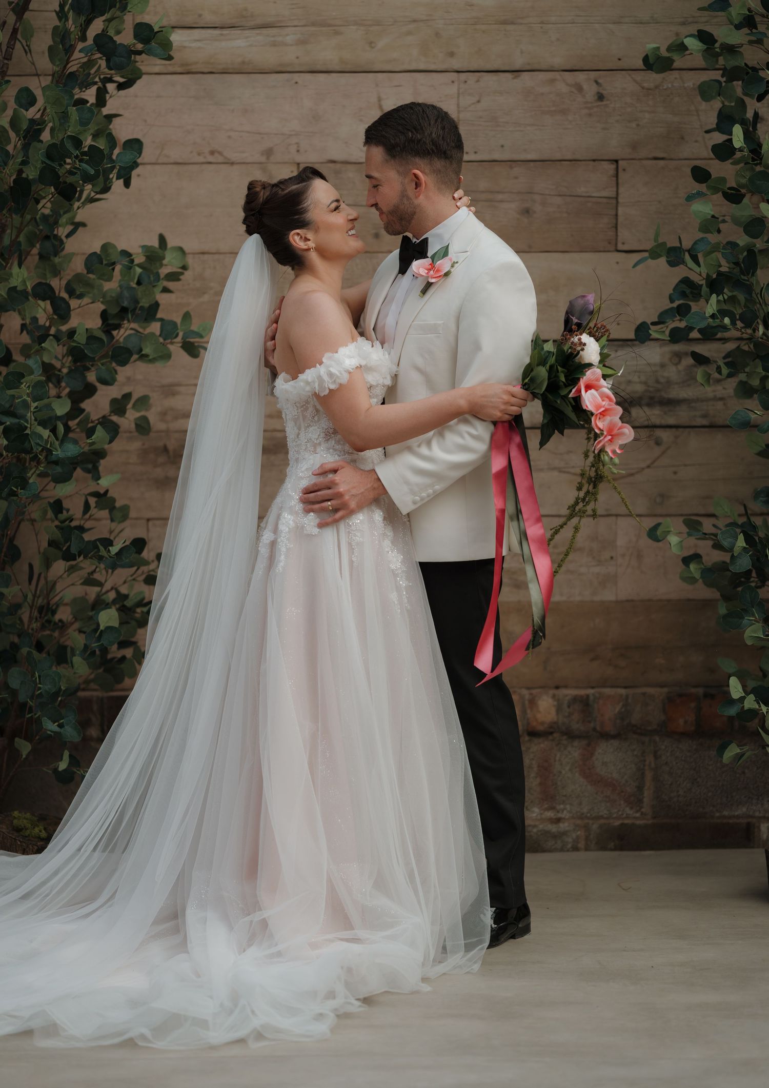 A romantic wedding couple embraces in front of a rustic wooden wall with cascading greenery. Derbyshire Wedding Photography