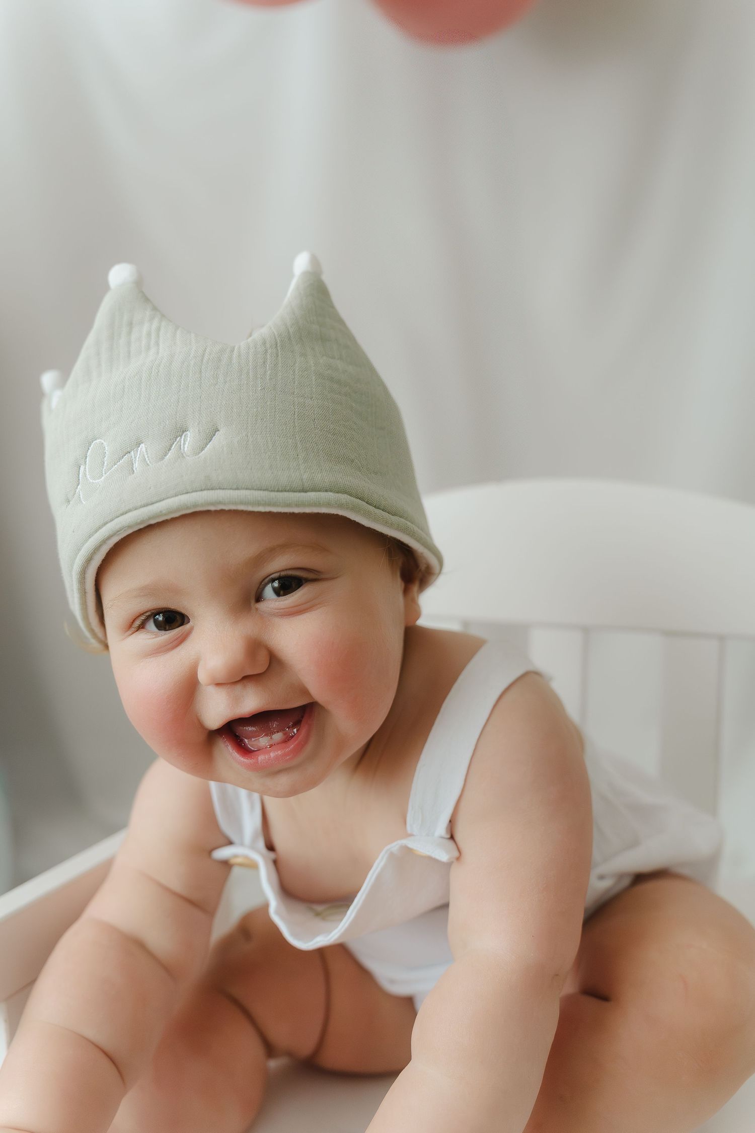 Baby wearing soft crown smiling joyfully in white outfit. Milestone Photography in Derbyshire