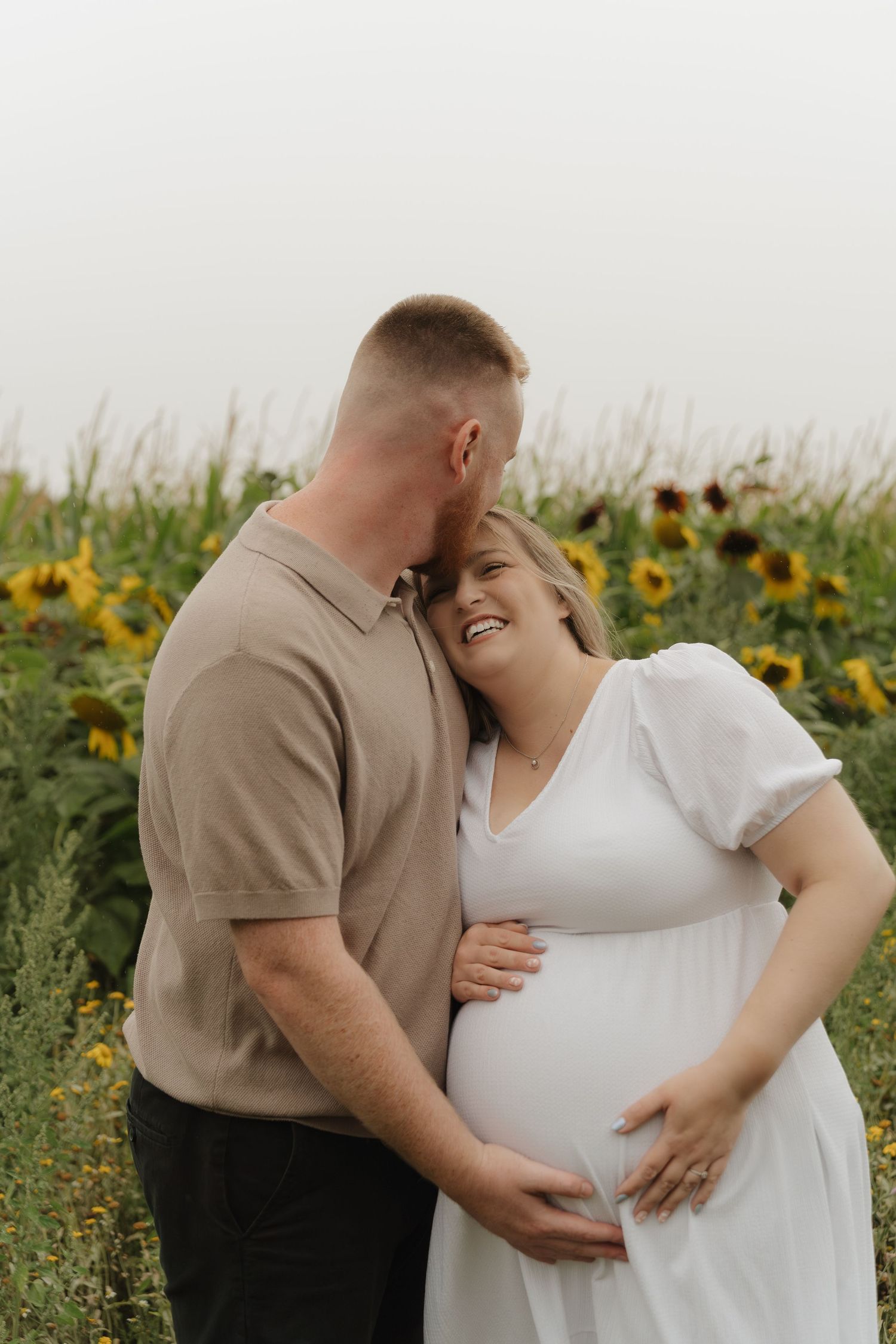 Romantic maternity photoshoot in a wildflower field shows tender moments between couple at sunset.