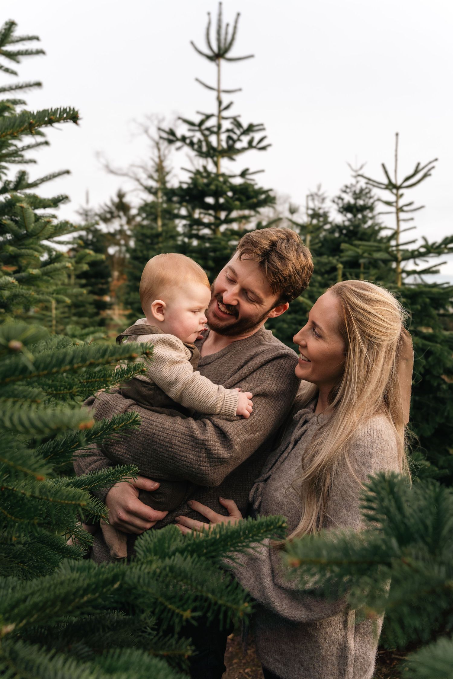 Family shares loving moments and laughter while surrounded by pine trees at a Christmas tree farm.
