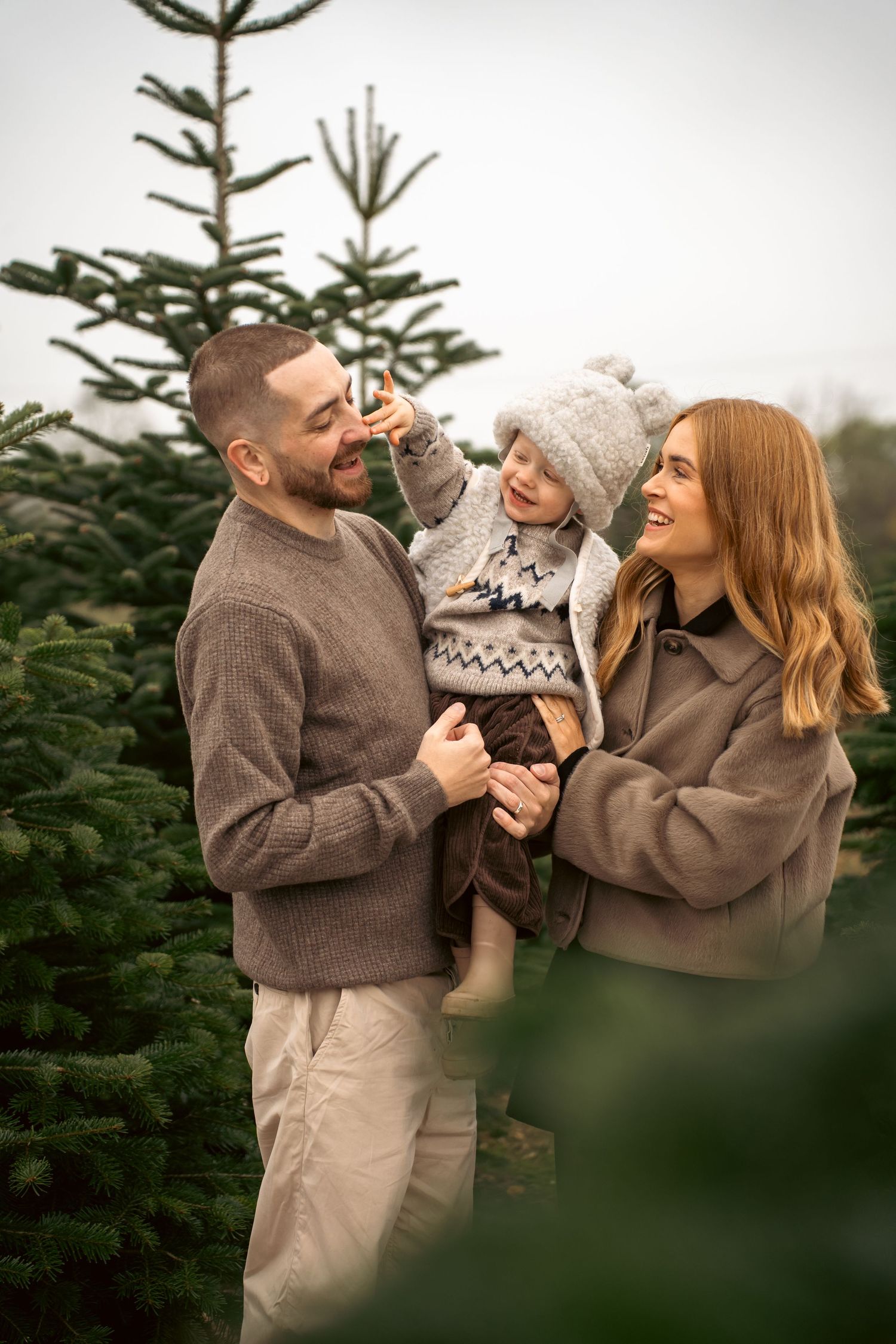 A happy family shares joyful moments together among evergreen trees during a winter photo session.