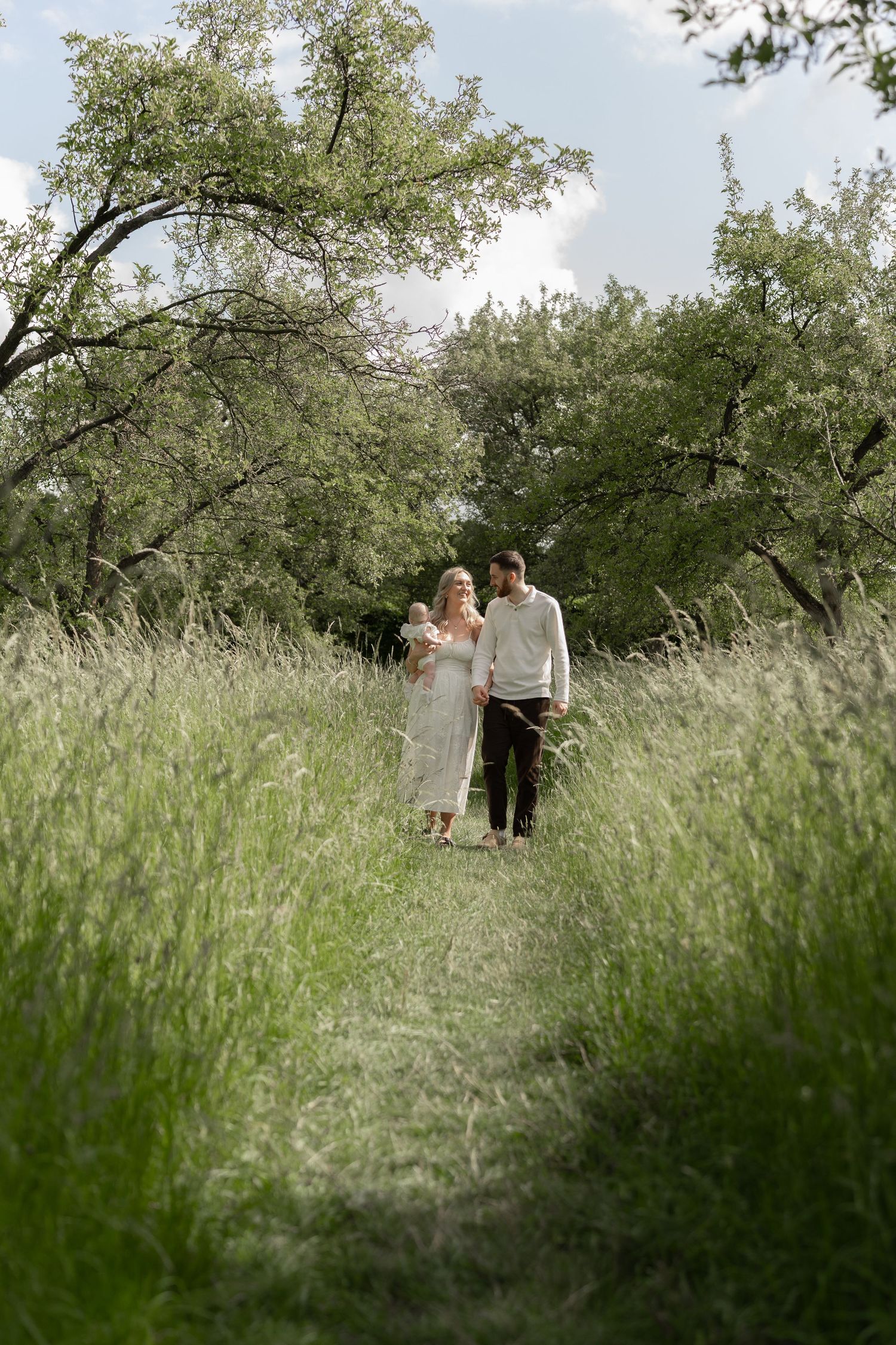 A couple shares an intimate moment in a dreamy meadow surrounded by tall grass and blooming trees.