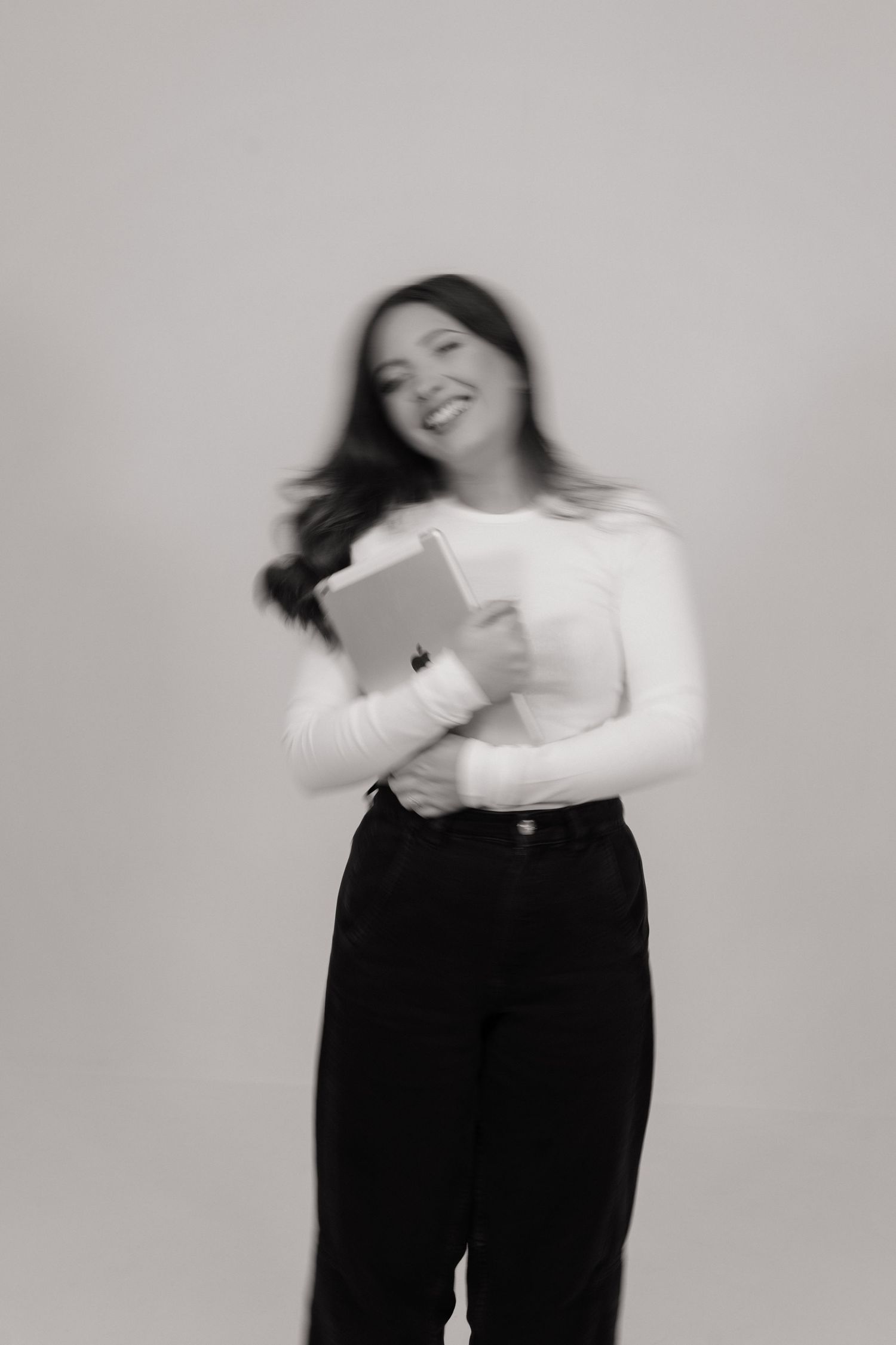 Black and white photo of smiling woman holding a tablet in a white long sleeve top and black pants.