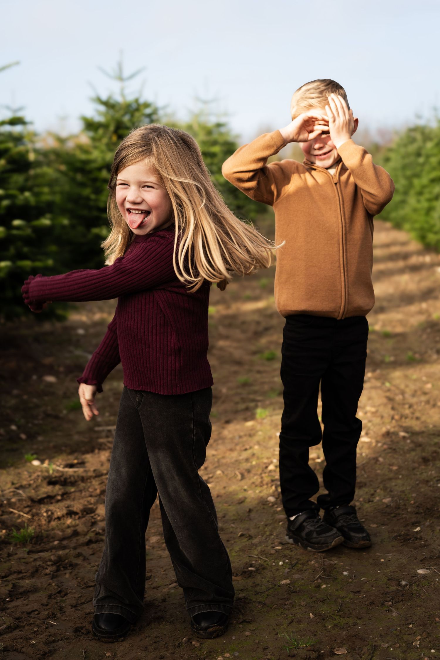 Two children playing and laughing together outdoors on a dirt path surrounded by greenery.