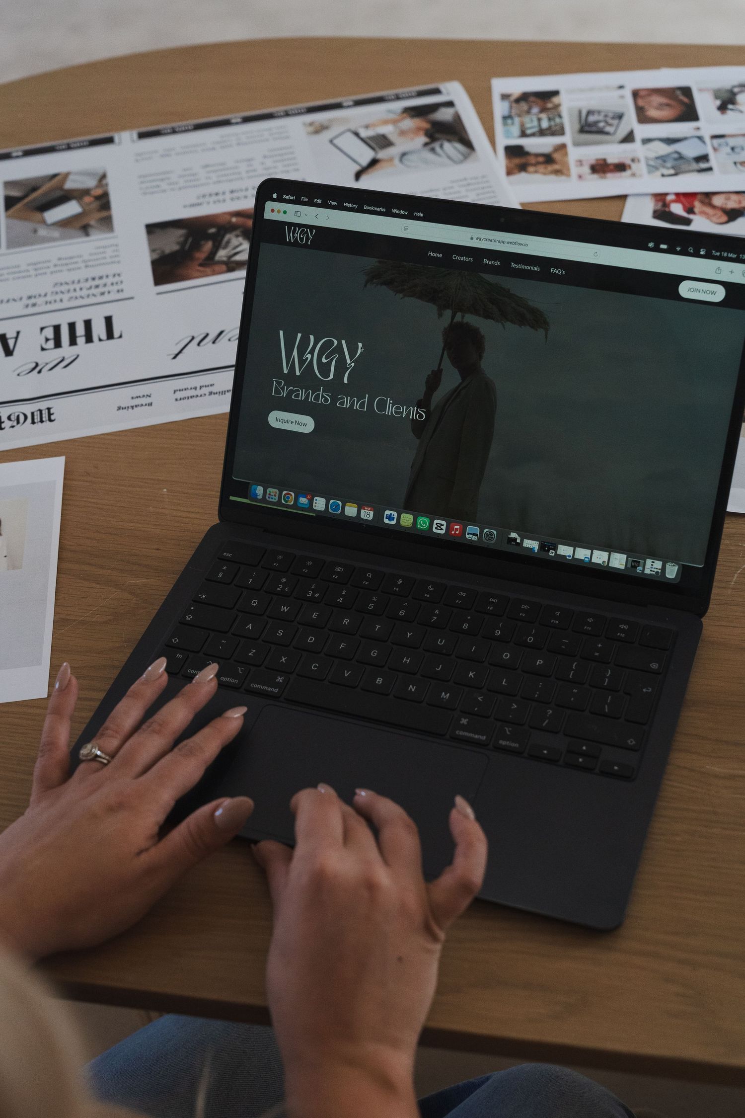 Hands typing on a black keyboard while working at a wooden desk with documents spread out.