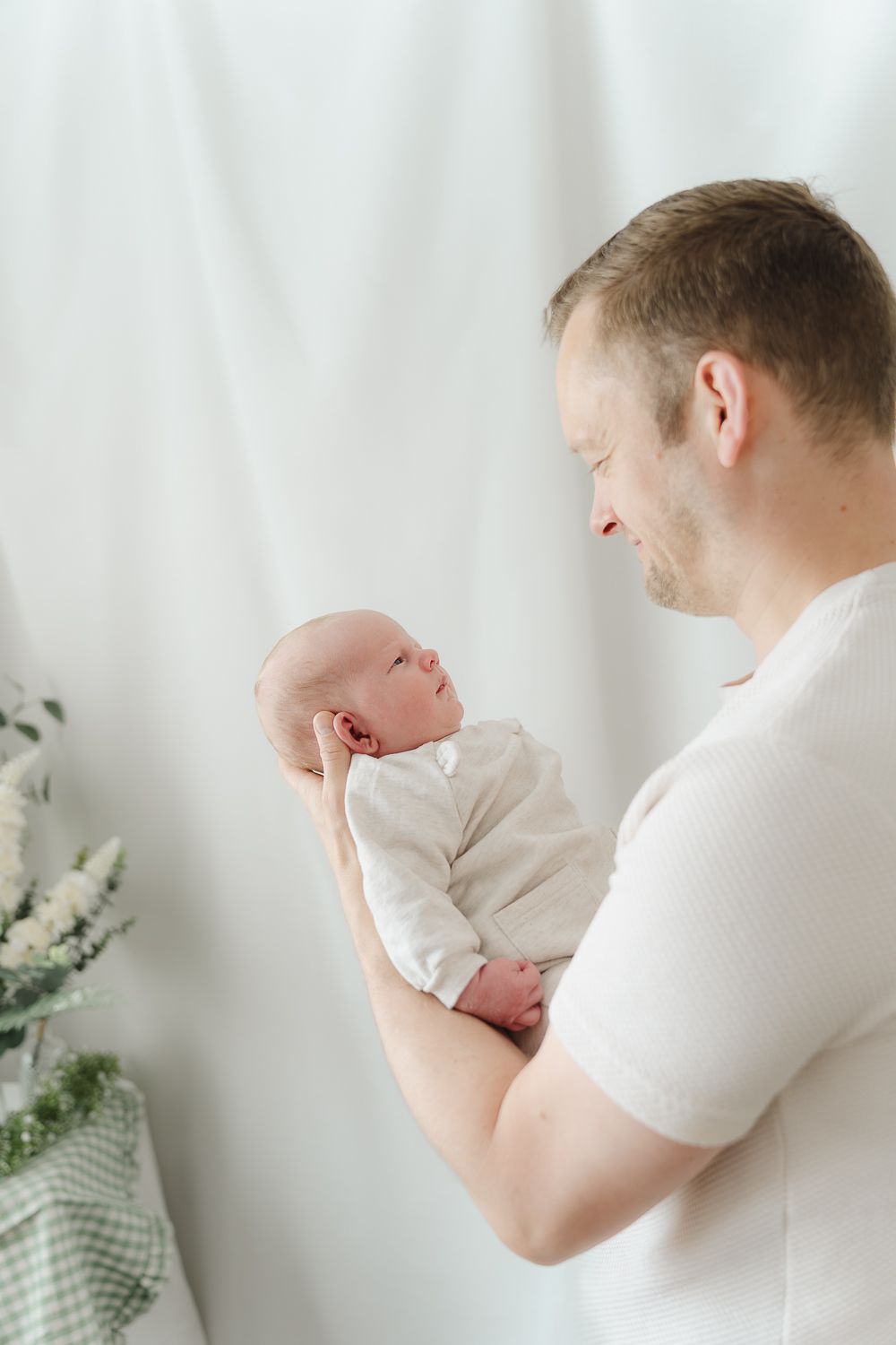 Gentle parenting moments captured in white tones as adults hold a small baby.
