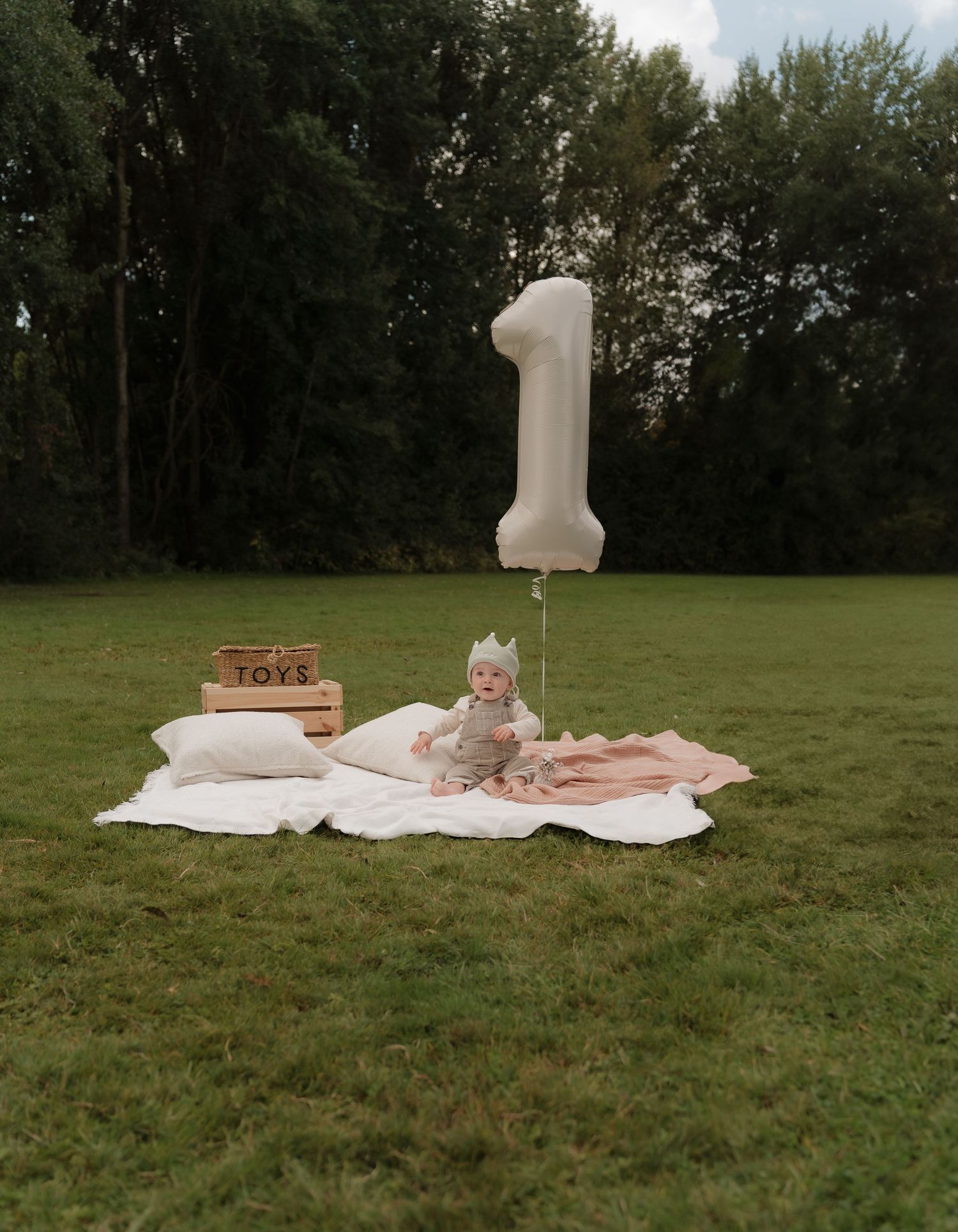 White blanket and decorative items arranged on green grass for outdoor photoshoot.