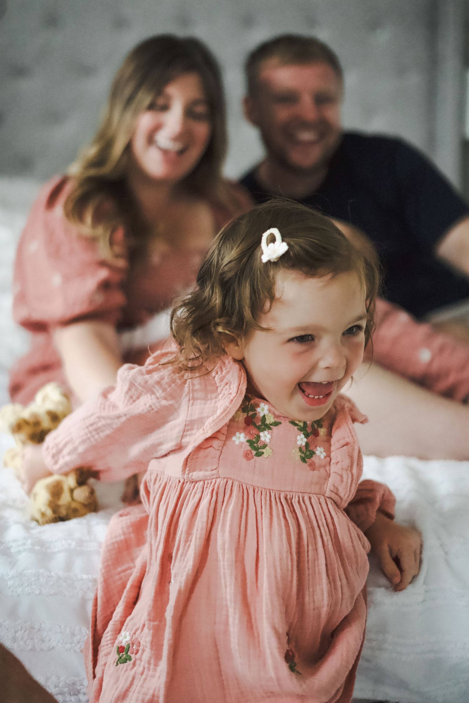 A child in a pink dress playing and laughing during a family photoshoot.