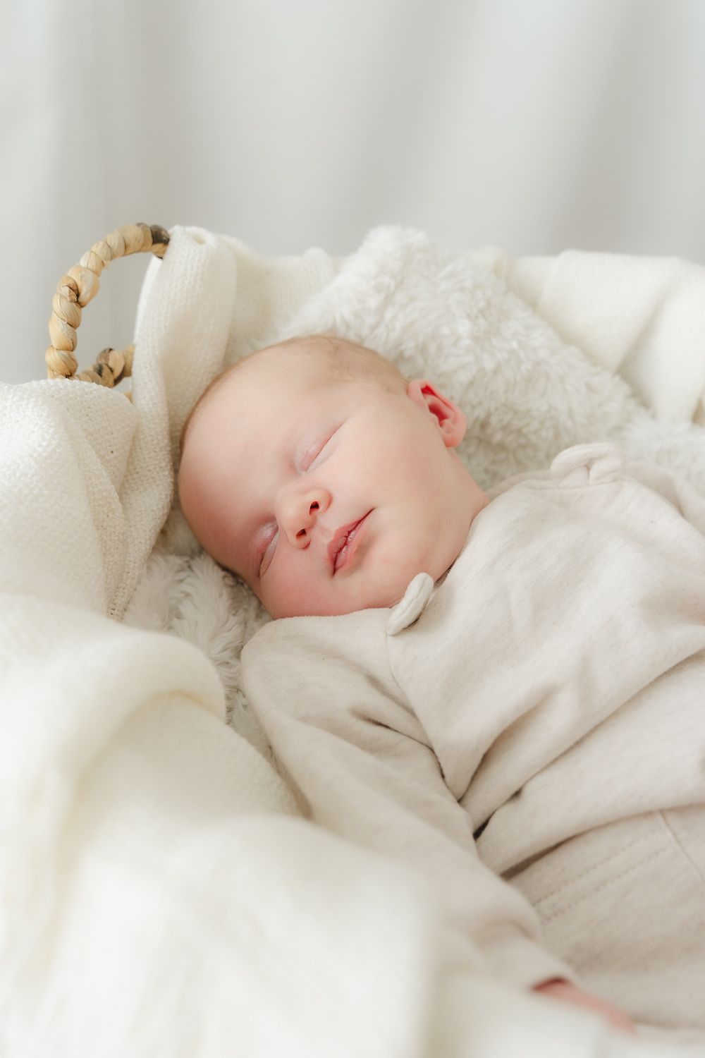 Peaceful sleeping baby in soft white clothing against light background.