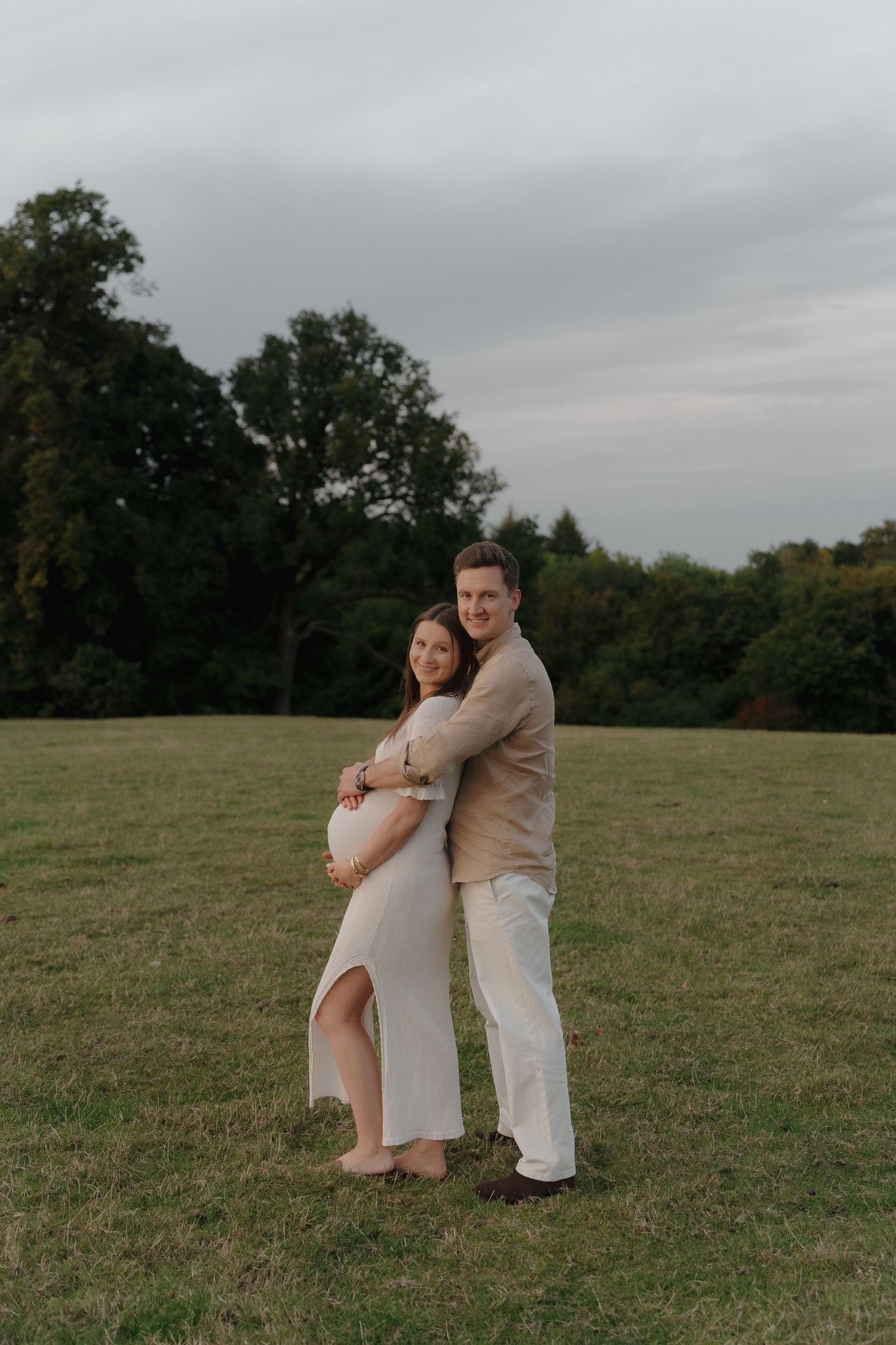 A couple shares an intimate embrace in a grassy field on an overcast day.