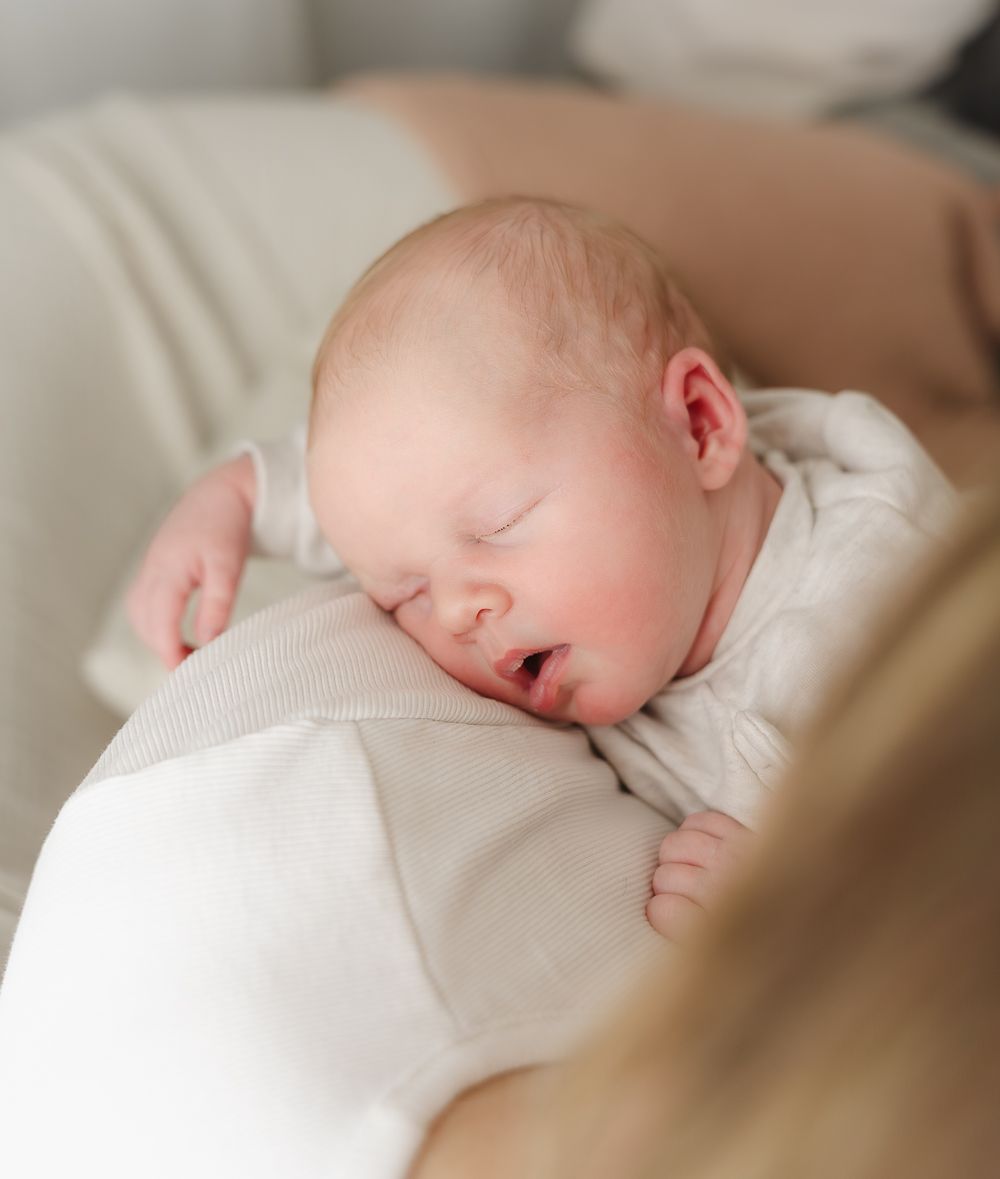 A sleeping infant in white clothing rests peacefully on cream-colored fabric.