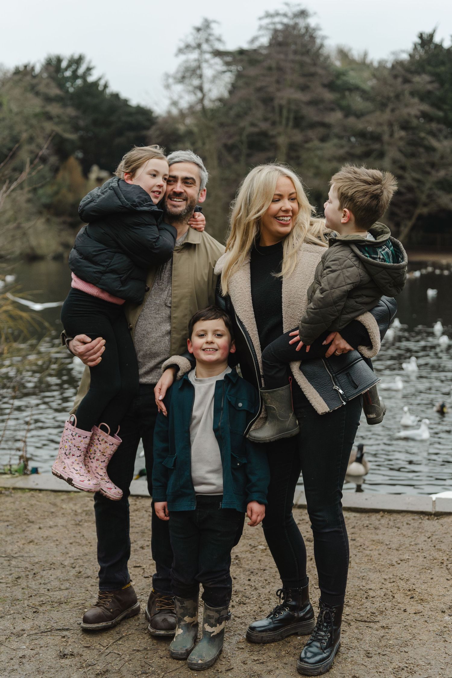 Family of five enjoying outdoor time by a lake on cloudy day.