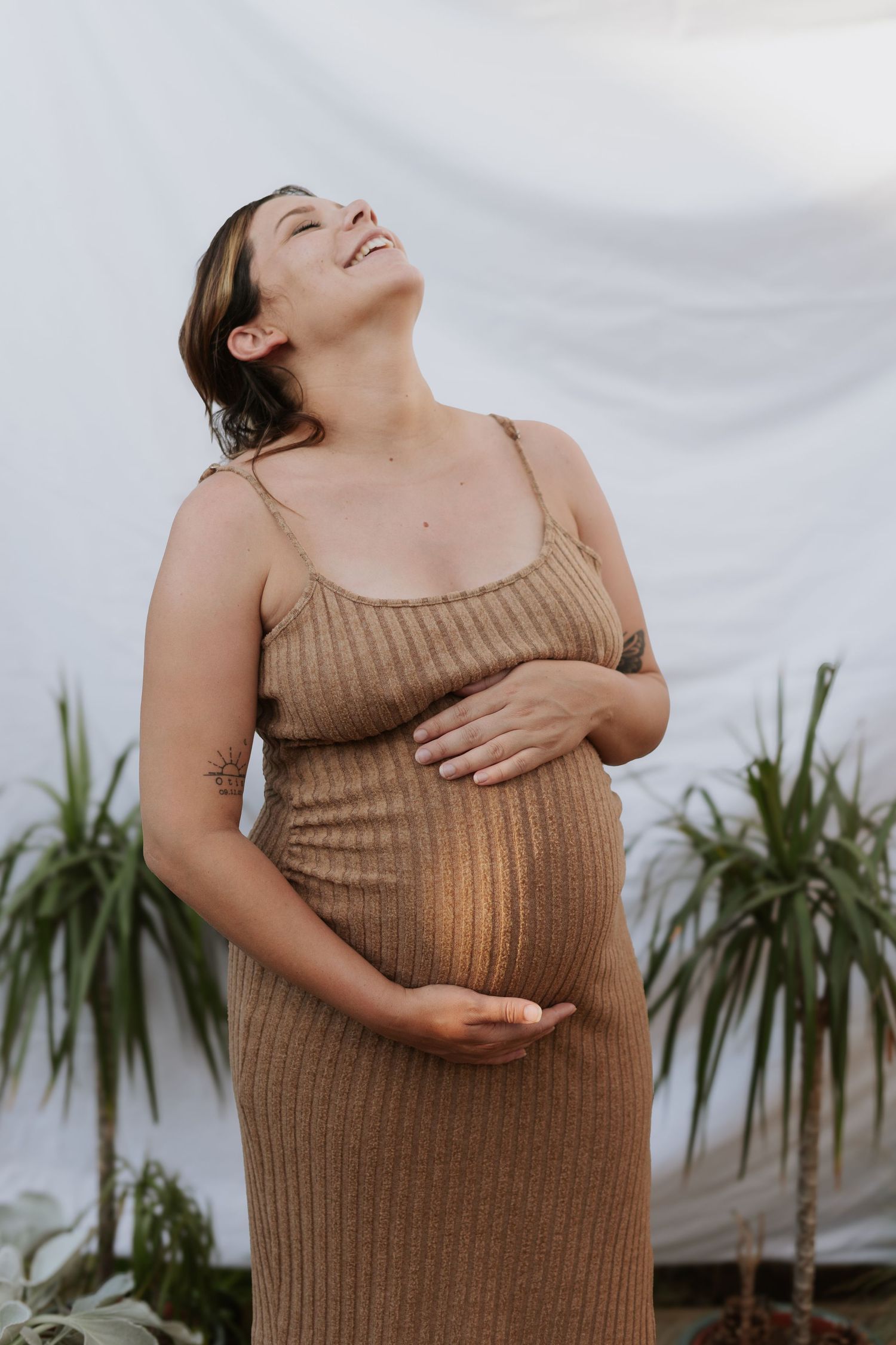 Expectant mother in brown dress smiling with joy while holding her belly.
