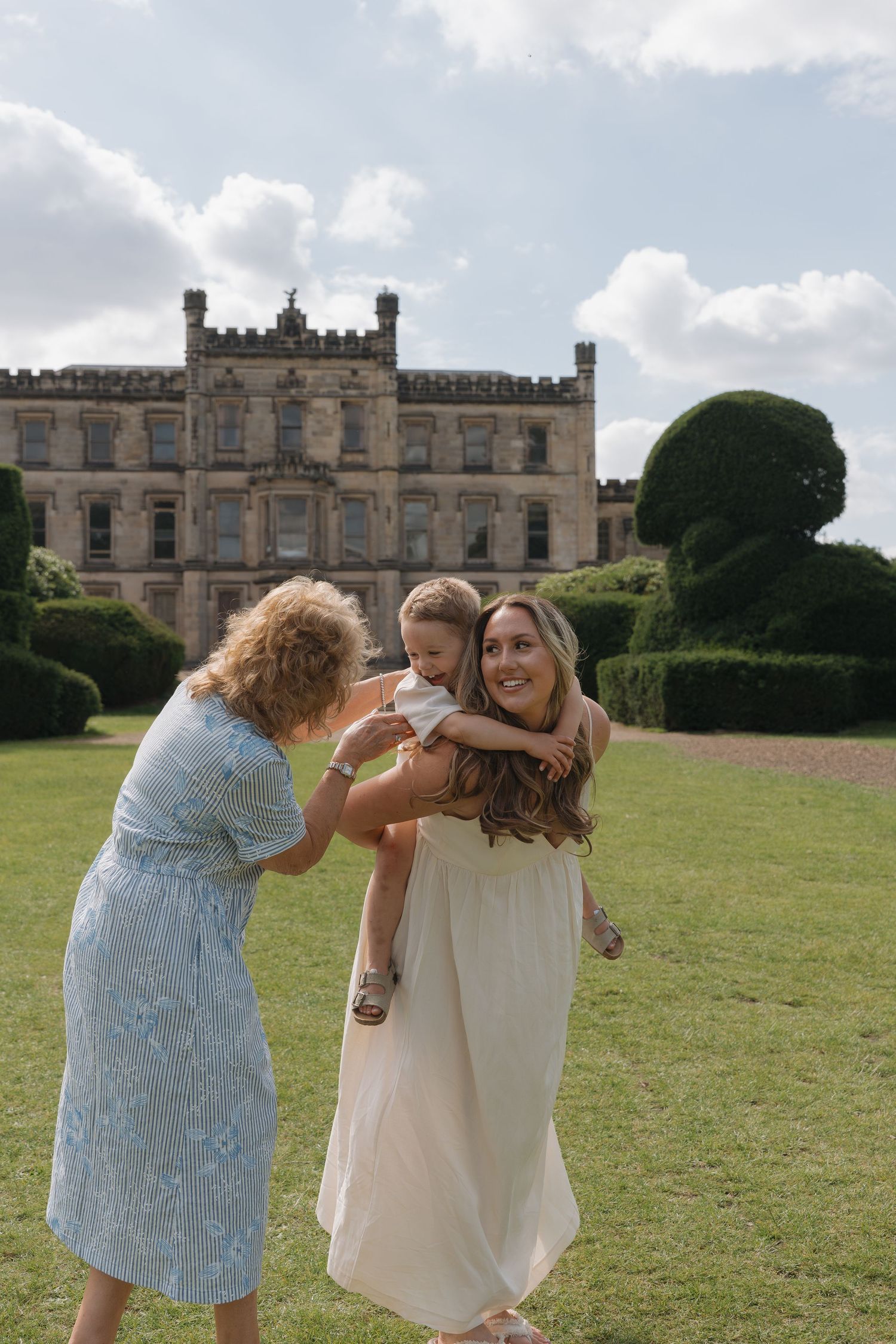 Two women and a toddler enjoying a sunny day on the lawn of a grand historic English manor house.