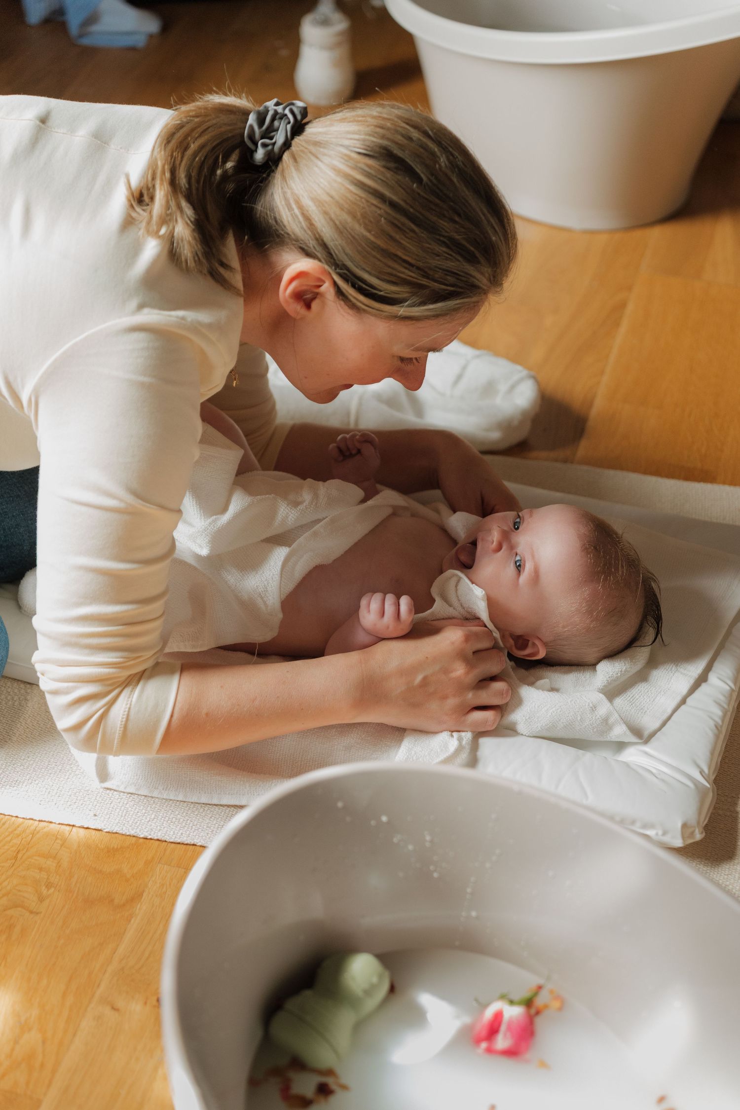 Mother tenderly caring for newborn baby on white changing mat after bath time at home.