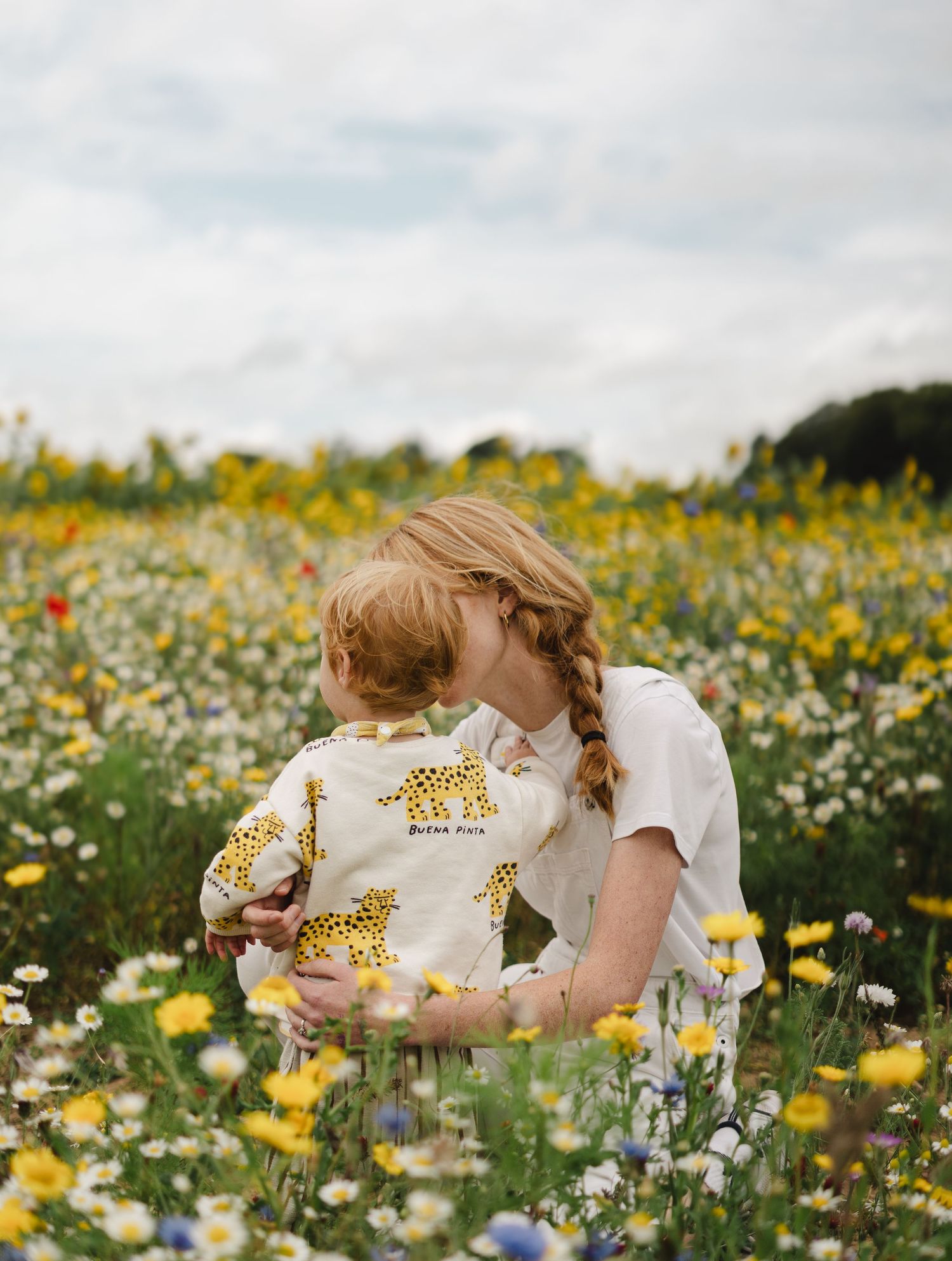 Parent and child sharing tender moment in wildflower meadow filled with yellow blooms.