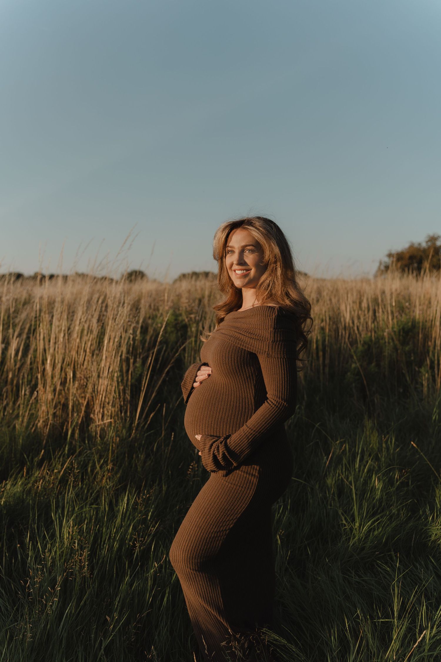 A maternity photoshoot in a field of tall grass at sunset.