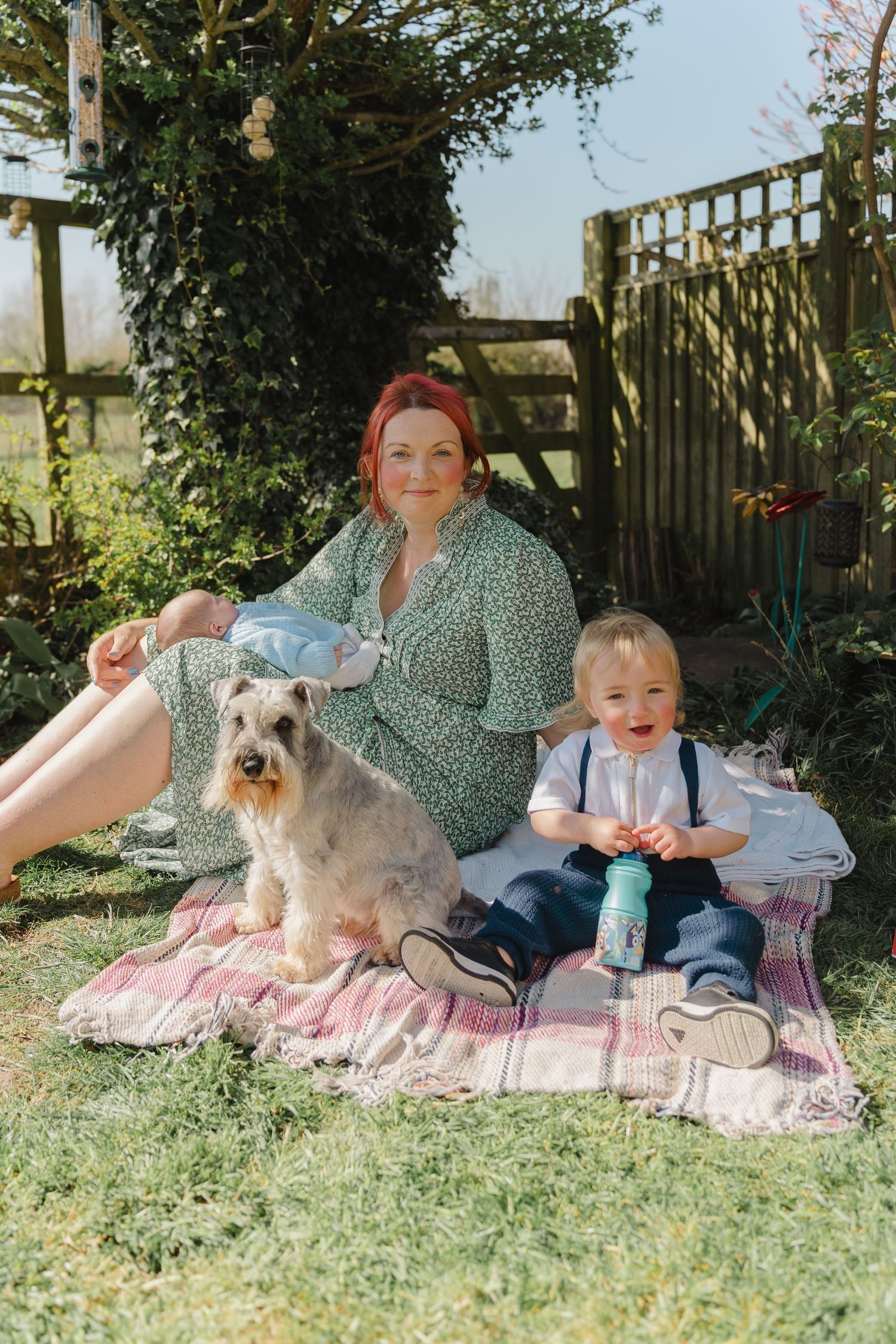 Family enjoying a spring picnic on a blanket with their fluffy white dog in a garden setting.